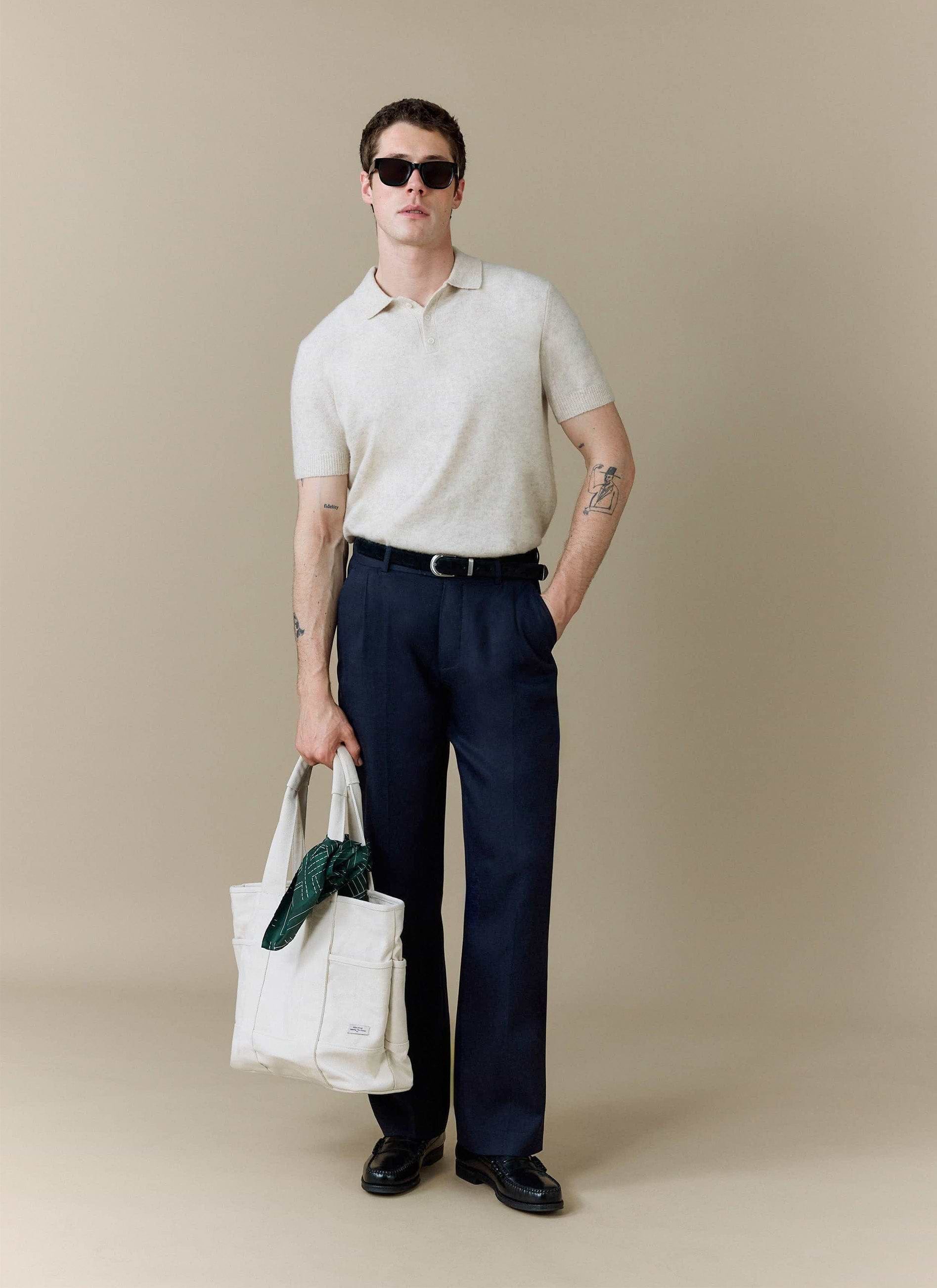 A model wears the Percival Collins Boxy Knitted Polo in ecru, styled with dark trousers, sunglasses, and a tote bag.