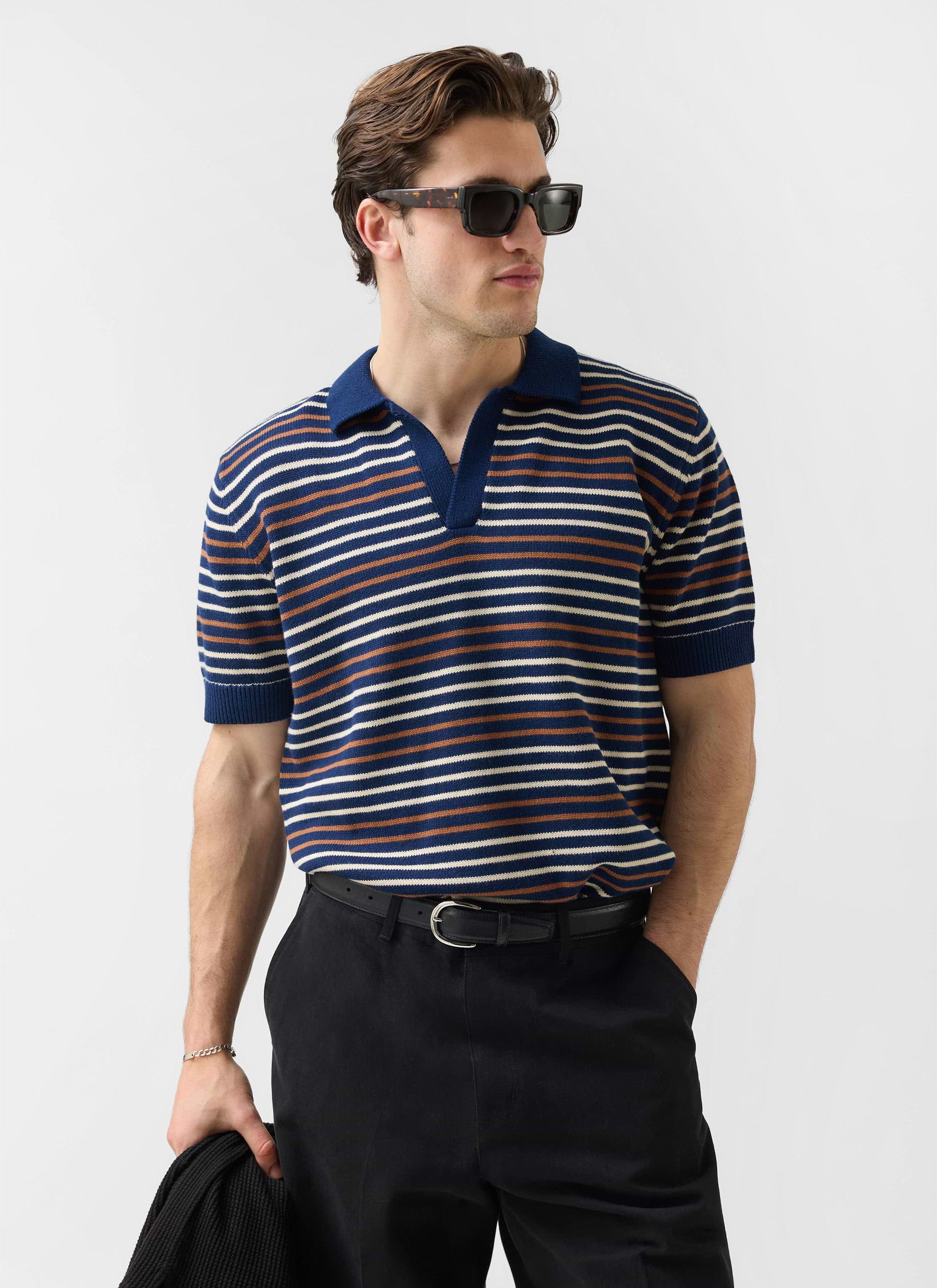A man models the navy striped Douglas Boxy Knitted Polo from Percival, wearing sunglasses and black trousers.