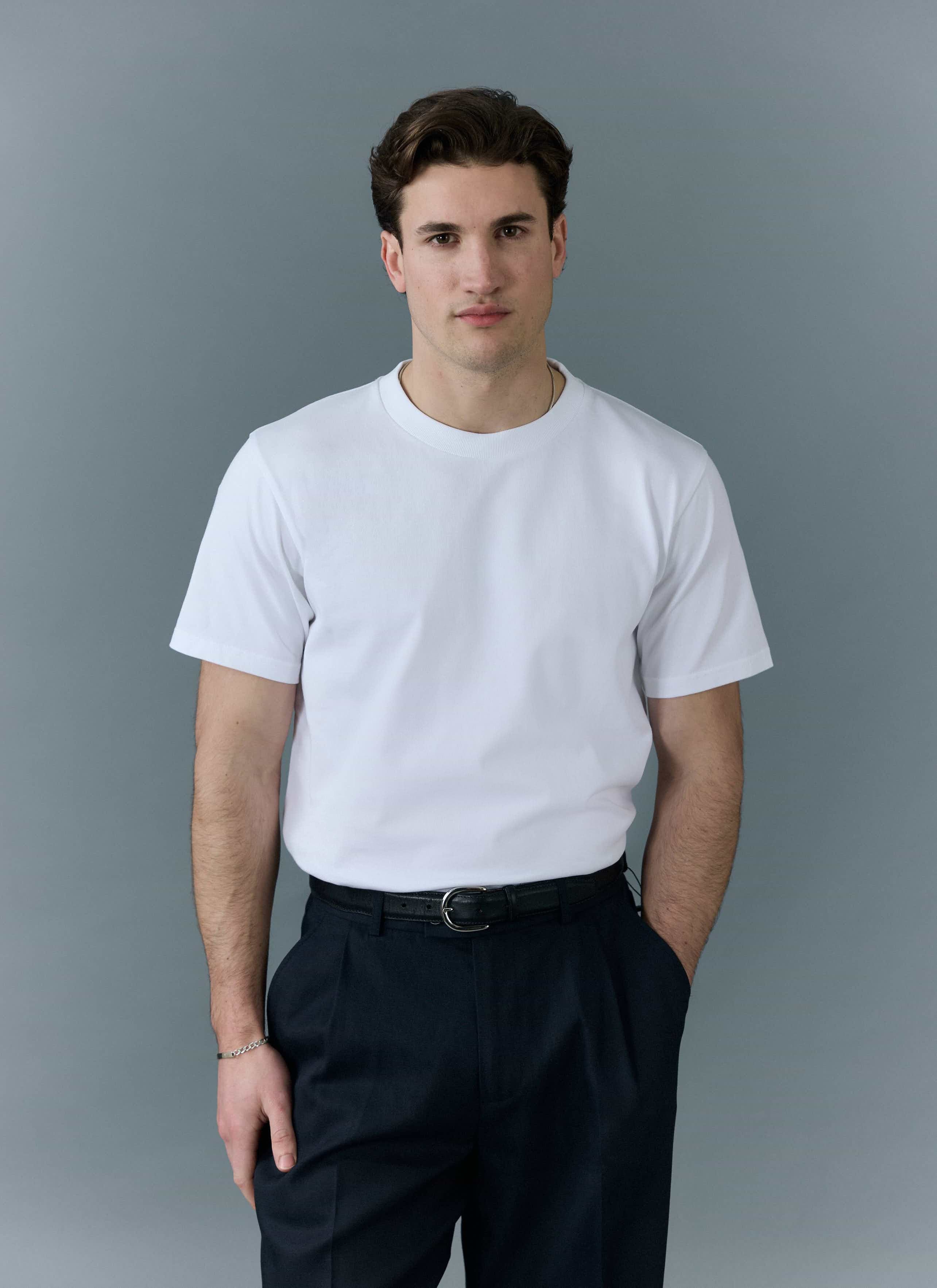 A model wears the Percival men's plain white organic cotton t-shirt with dark trousers against a grey background.