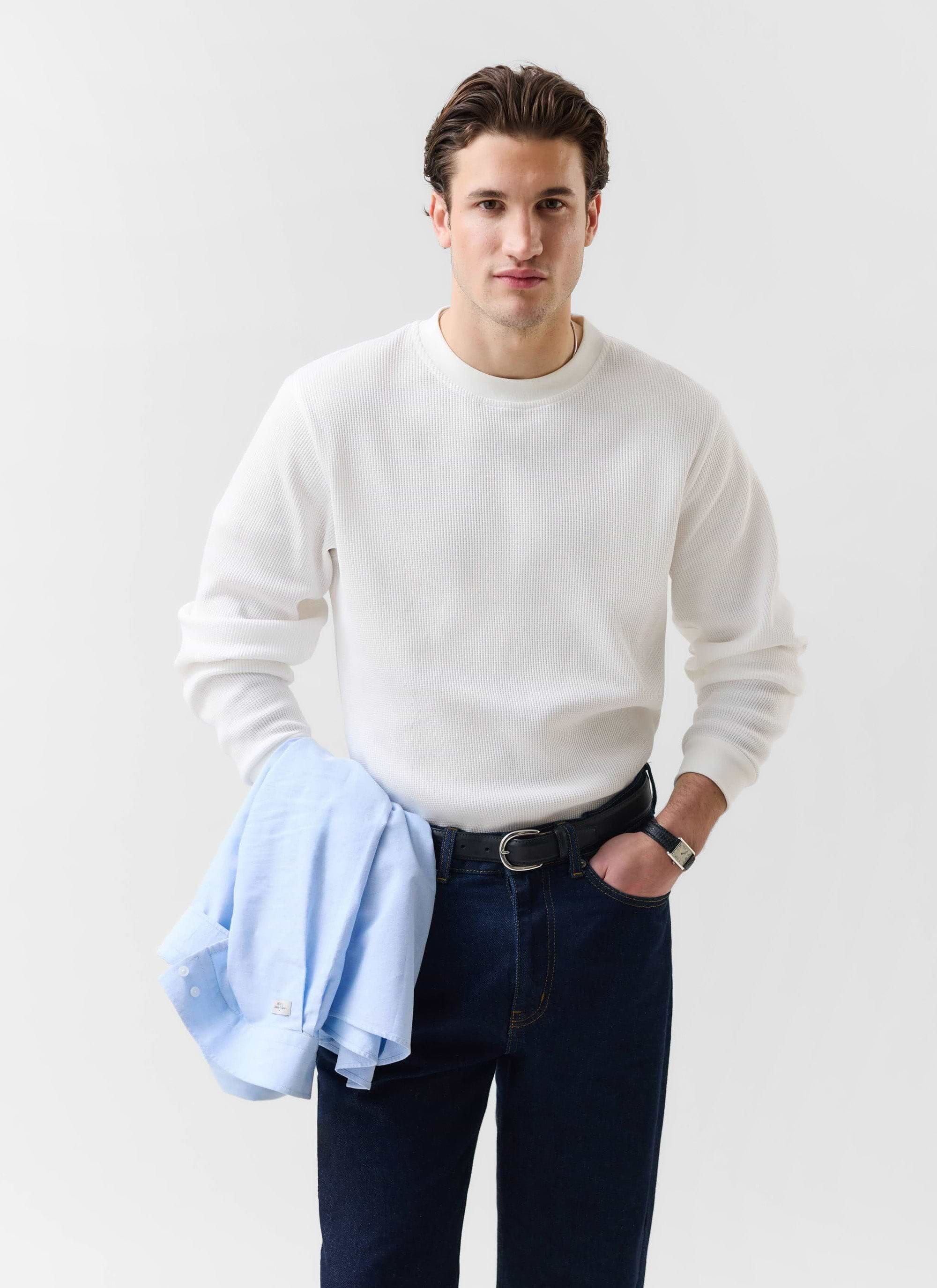 A male model wears the white Waffle Long Sleeve T-Shirt from Percival, styled with dark denim and holding a light blue shirt.