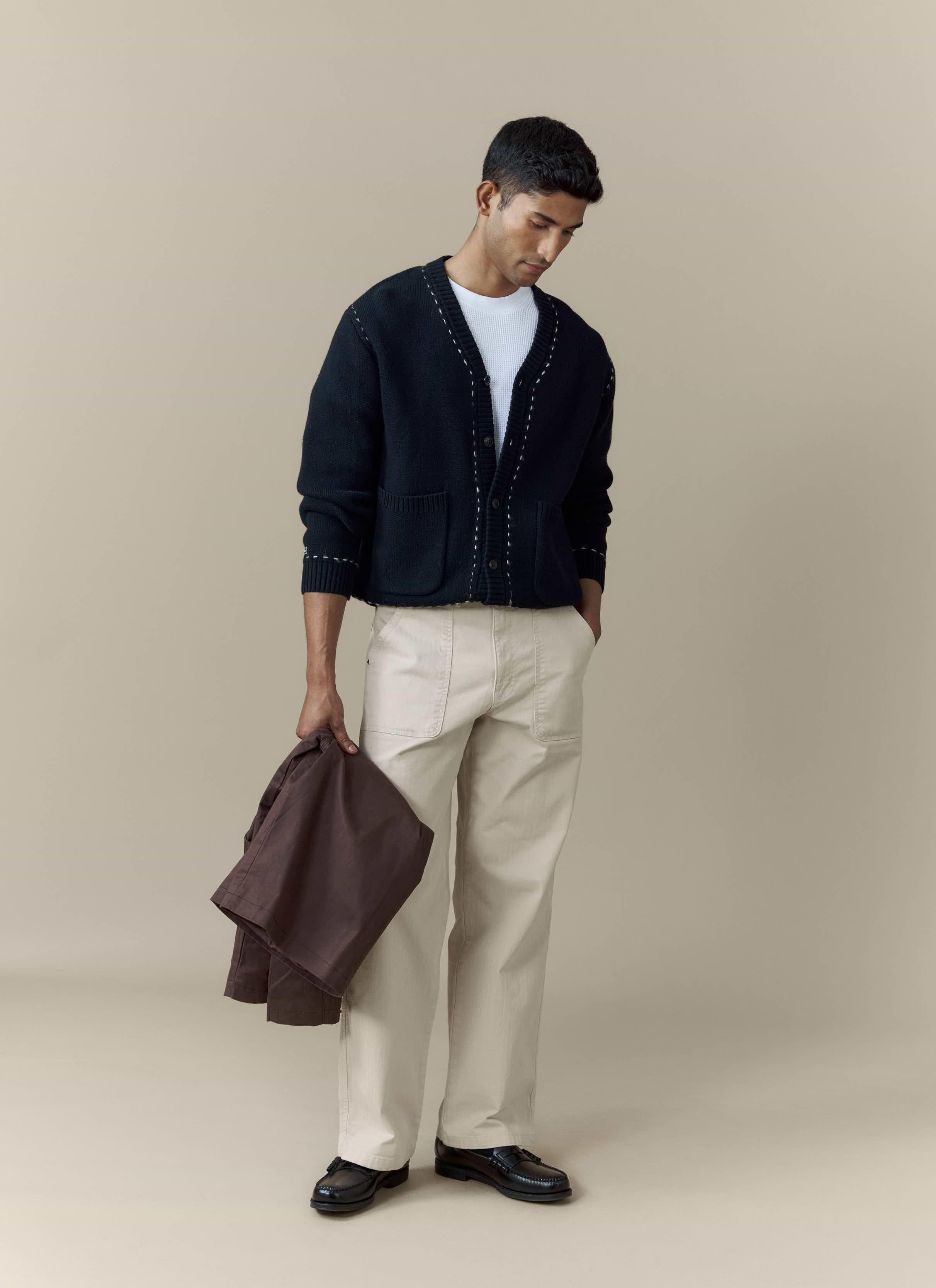 A man models the Percival Module Boxy Cardigan in black, styled with a white tee and light-coloured trousers.