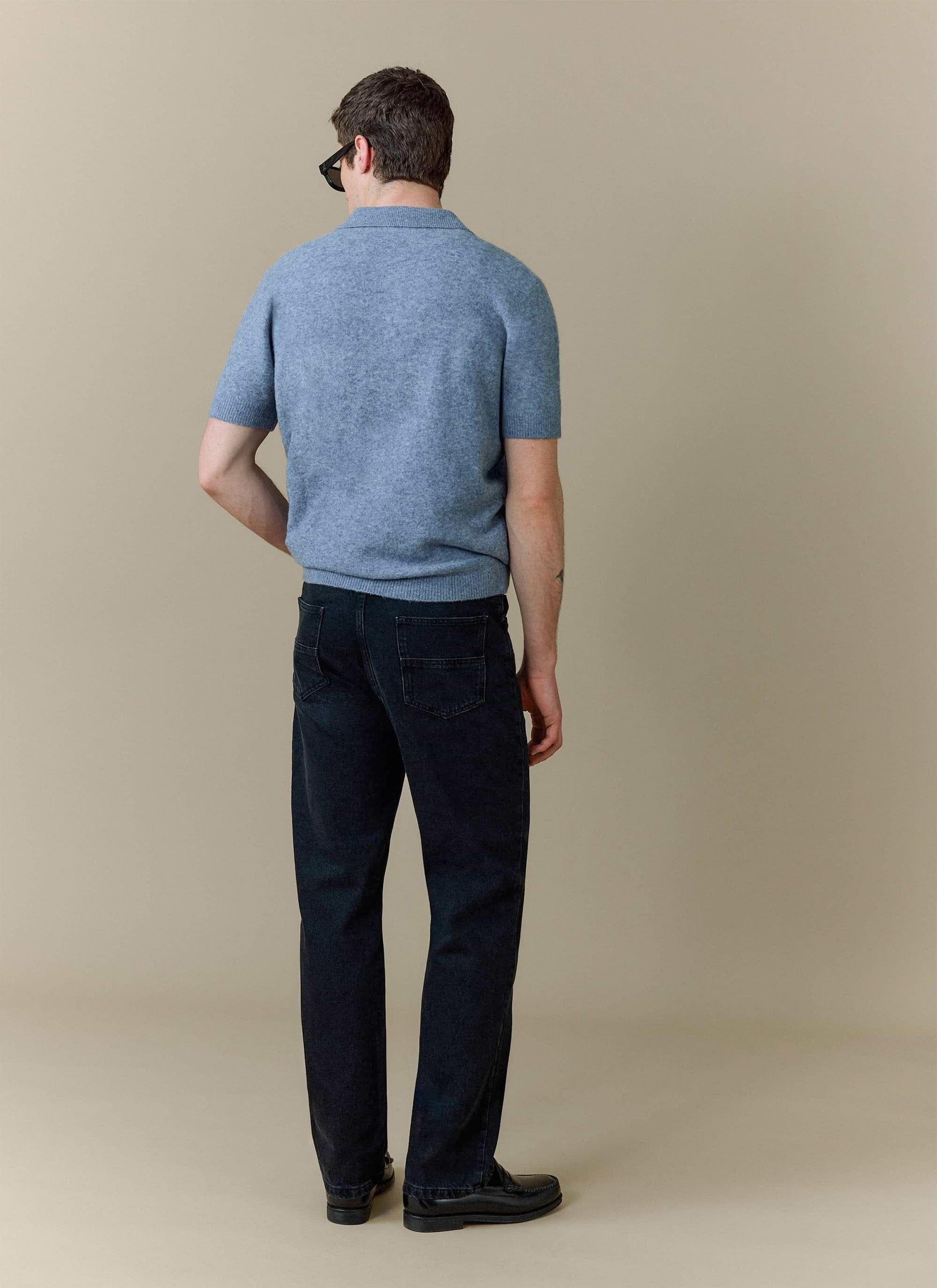 A model, shot from behind, wears the Percival Collins Boxy Knitted Polo in blue, styled with dark wash jeans.