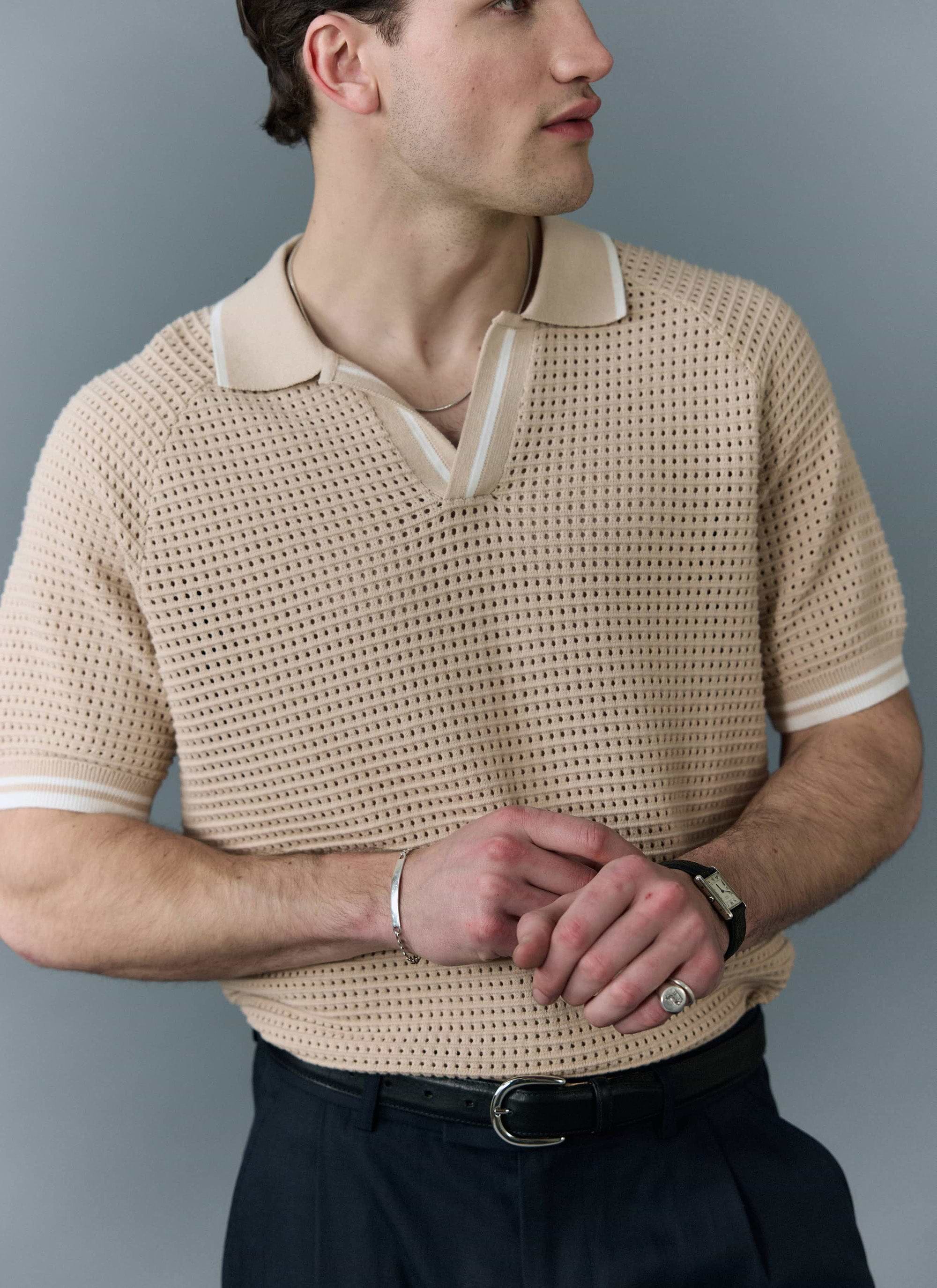 A man models the Percival Tennis Boxy Knitted Polo in ecru, showing the perforated cotton knit and striped open collar.