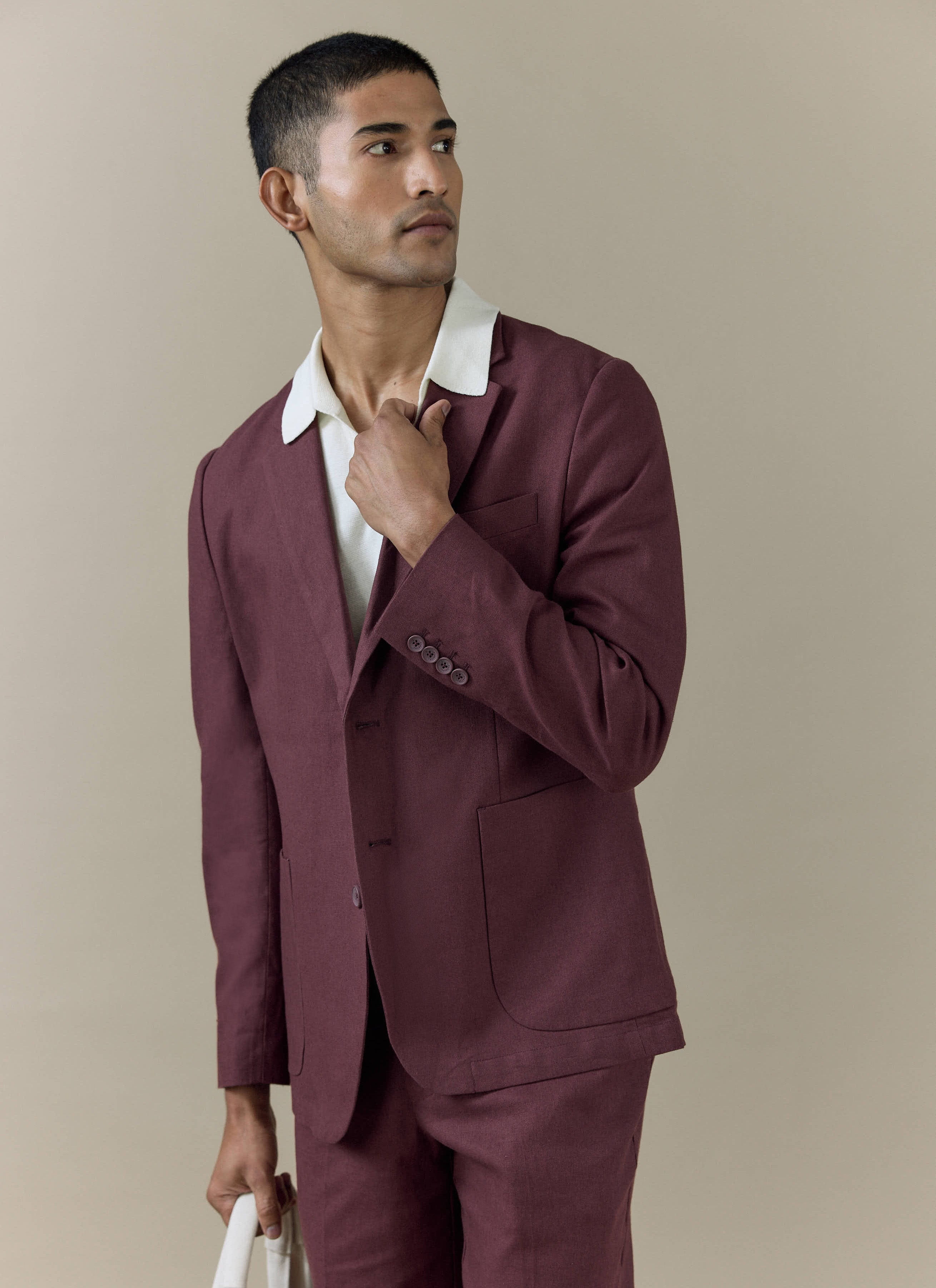 A model wearing the Percival tailored linen blazer in rich merlot burgundy, styled over a white collared knit shirt.