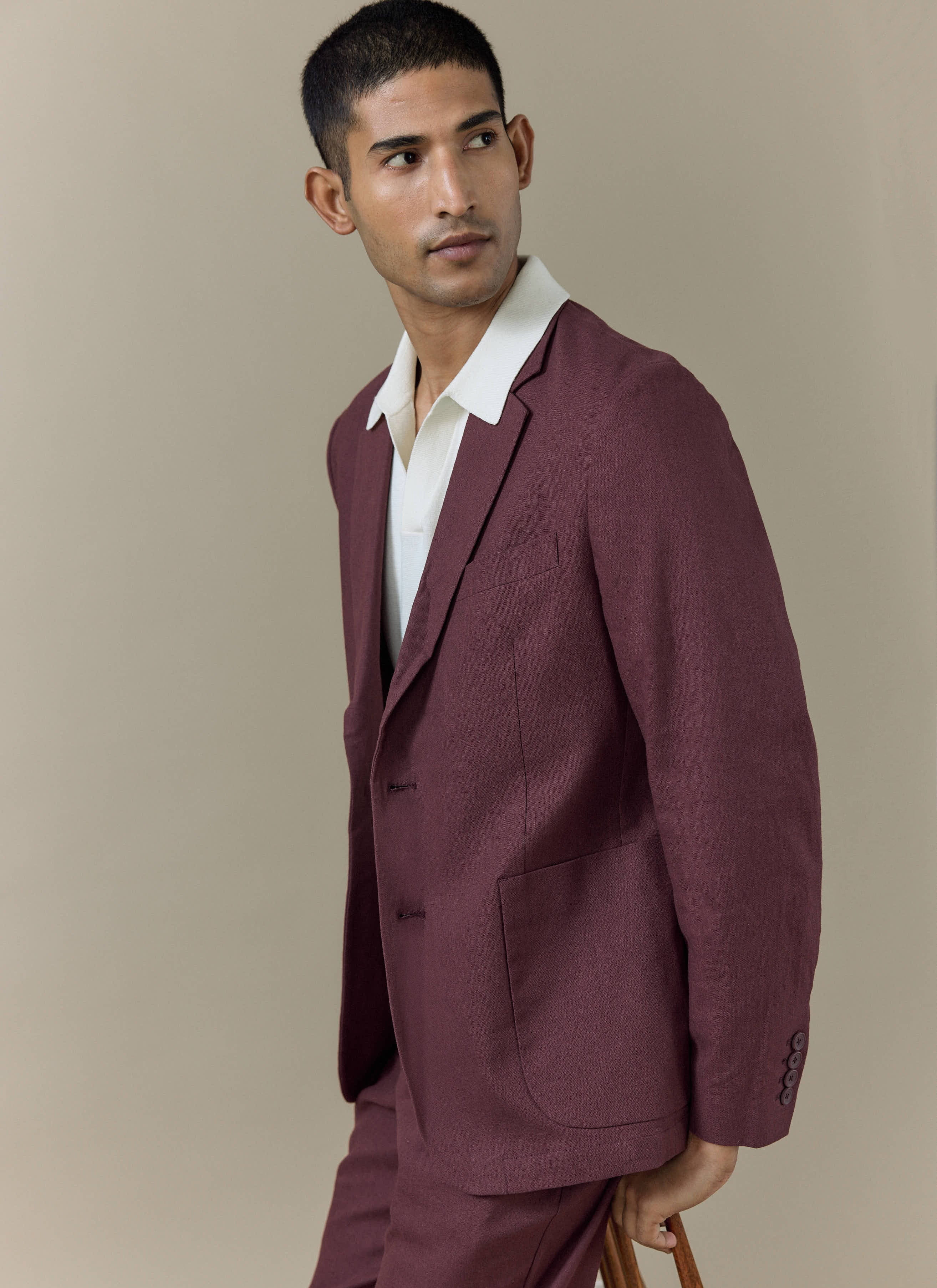 Cream Laurence Knitted Polo by Percival with a Johnny collar, layered under a tailored burgundy linen suit jacket.