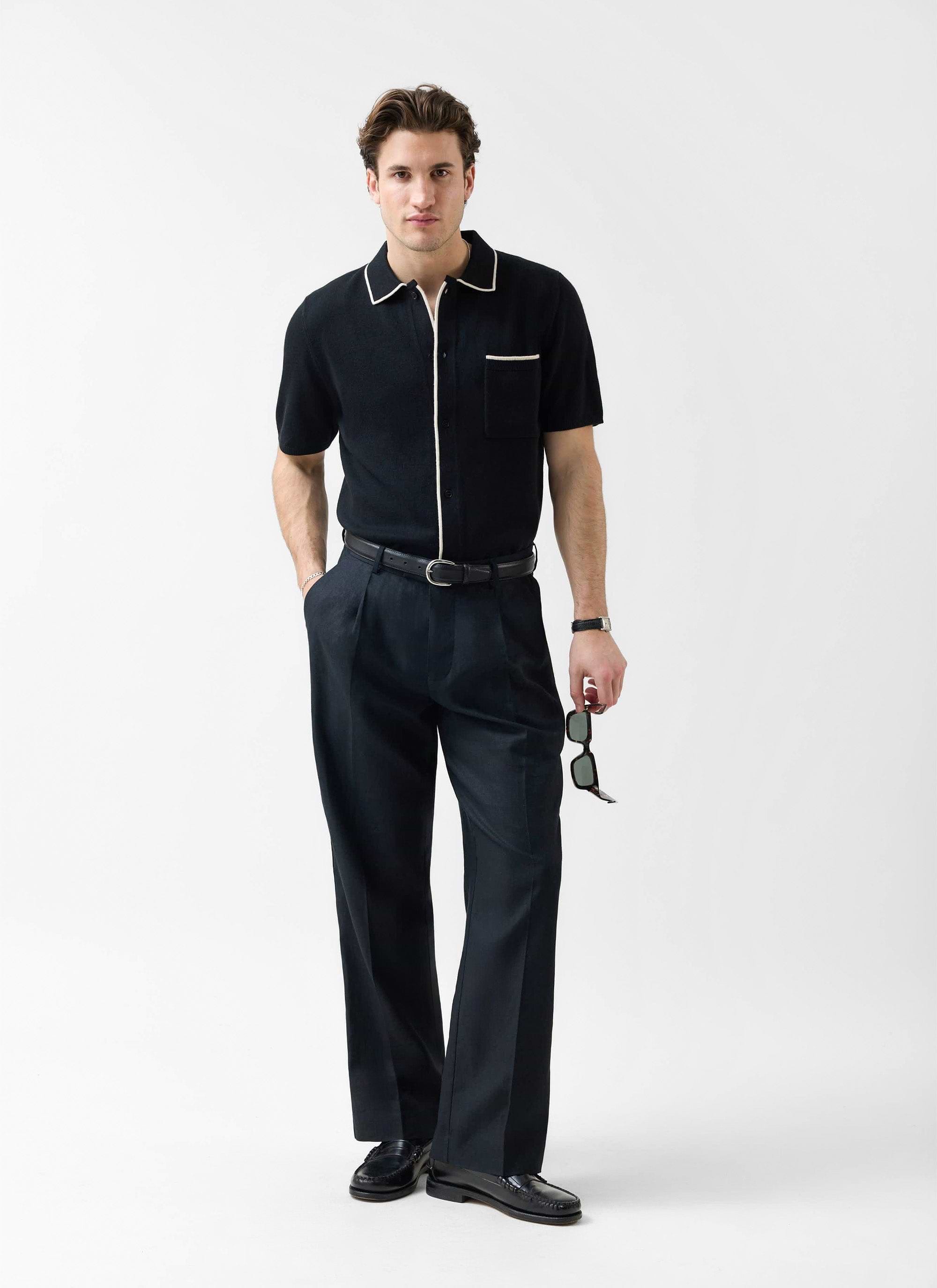 A model wears the black Percival Contrast Trim Regular Knitted Shirt with smart trousers and loafers in a studio setting.