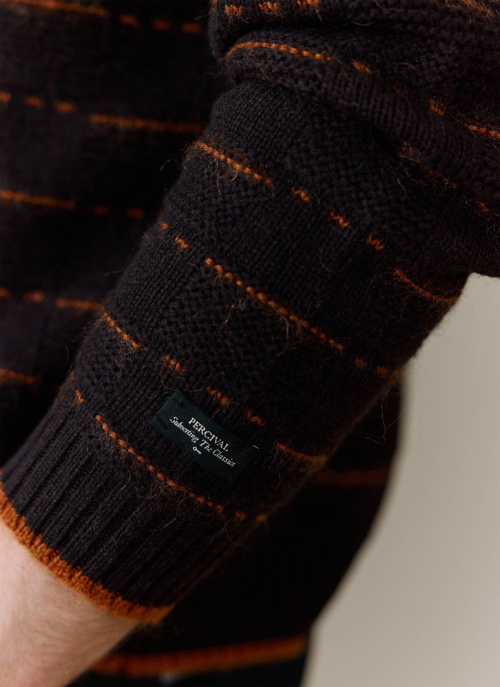 A close-up of the cuff on the brown wool Addison Knitted Shirt, showing the orange stitch detail and Percival label.
