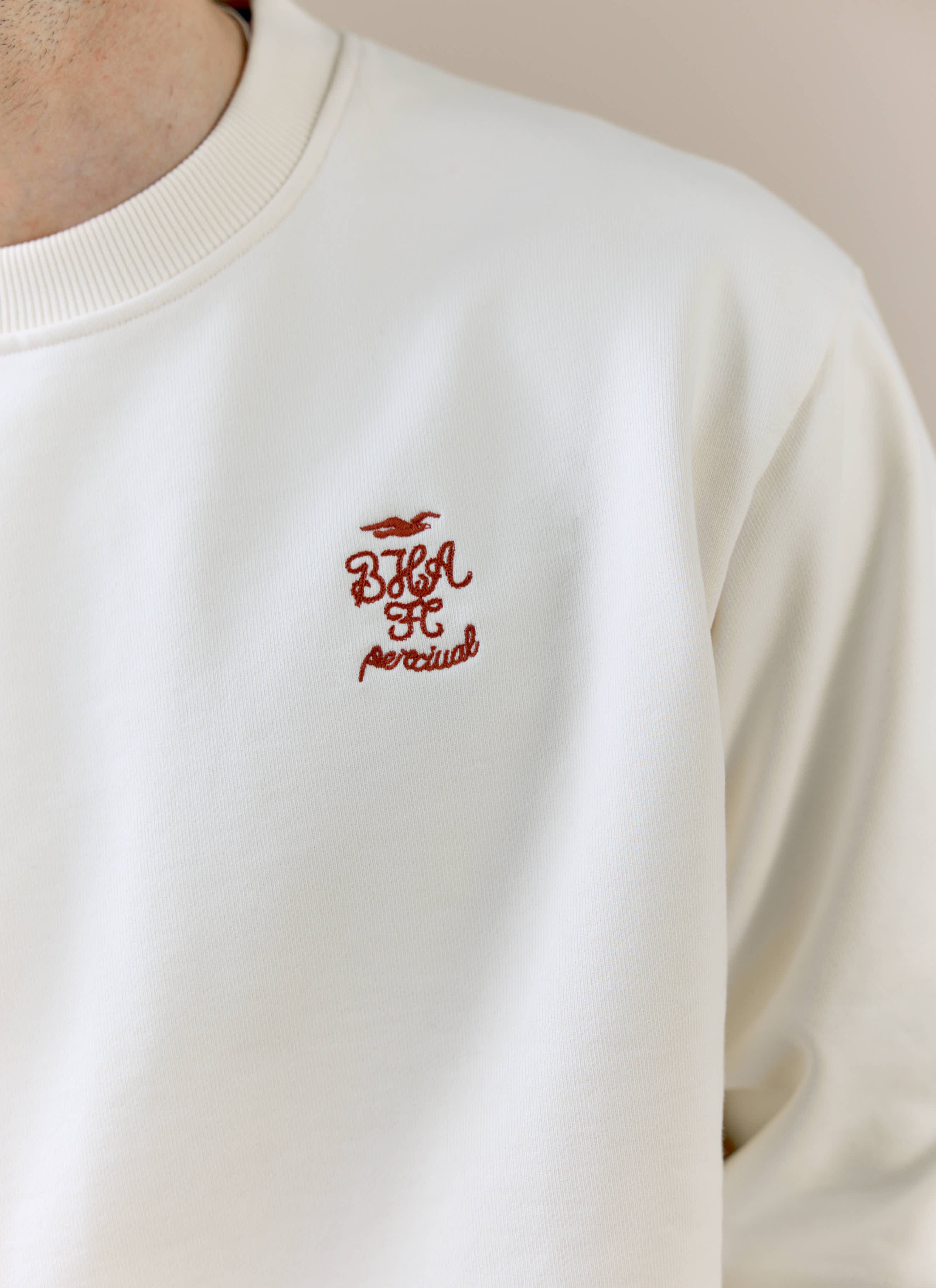 A detailed close-up of the embroidered chest logo on the cream Percival x Brighton & Hove Albion F.C. sweatshirt.