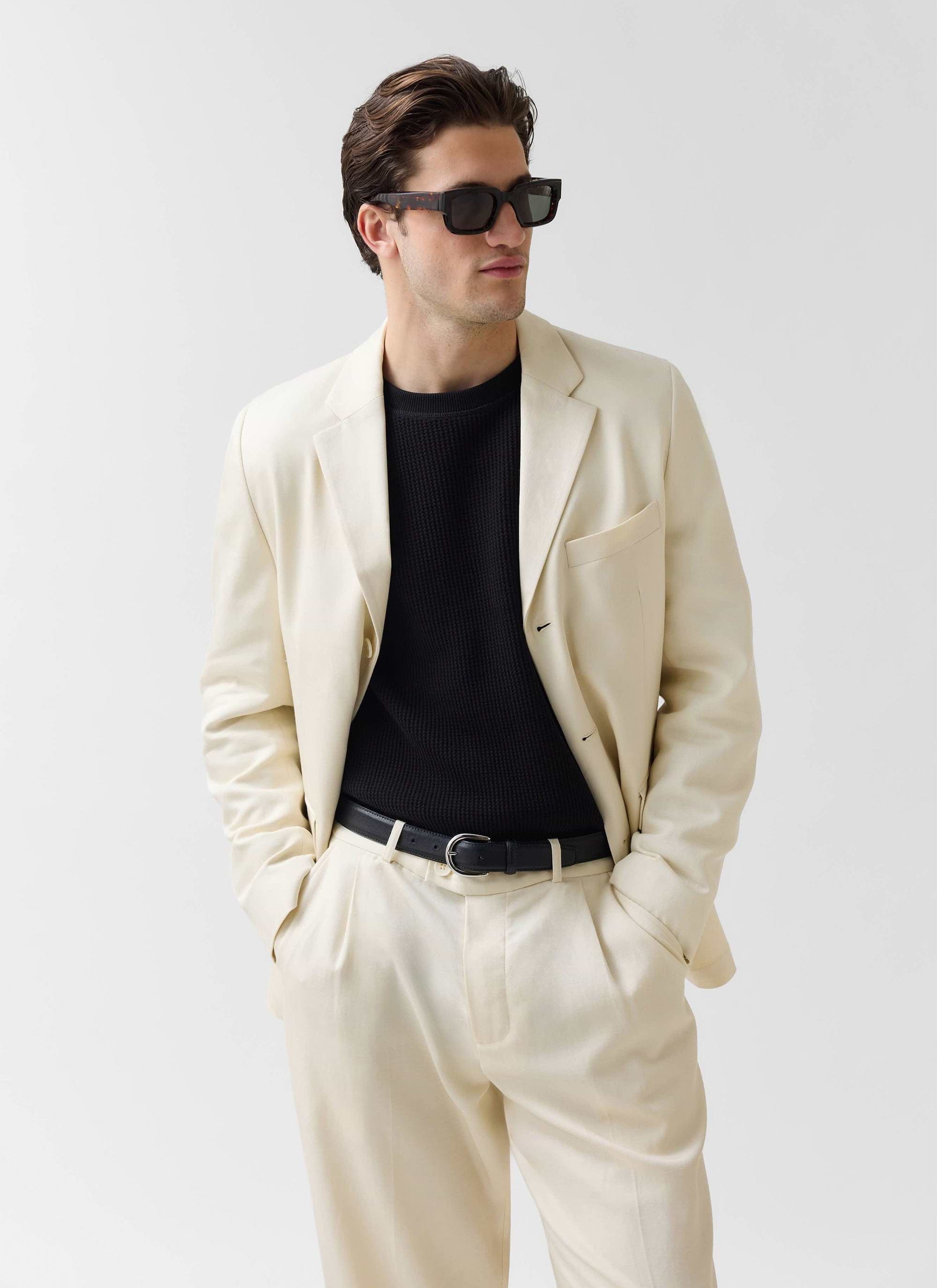 A model wears the Percival Clifton 3 Button Blazer in cream with matching trousers, a black knit jumper, and sunglasses.