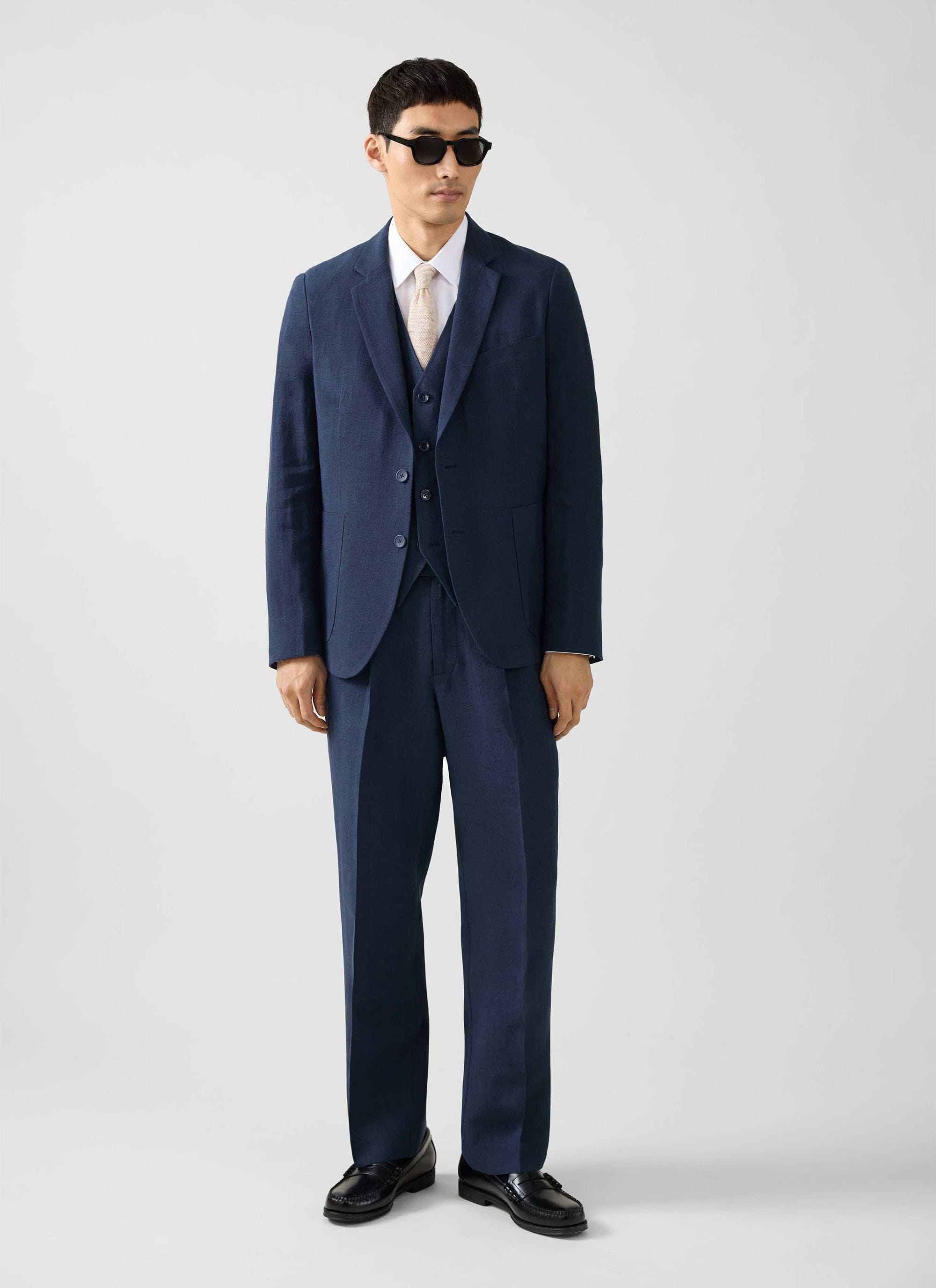 A model styles the Percival navy linen waistcoat as part of a three-piece suit with a cream tie and sunglasses.