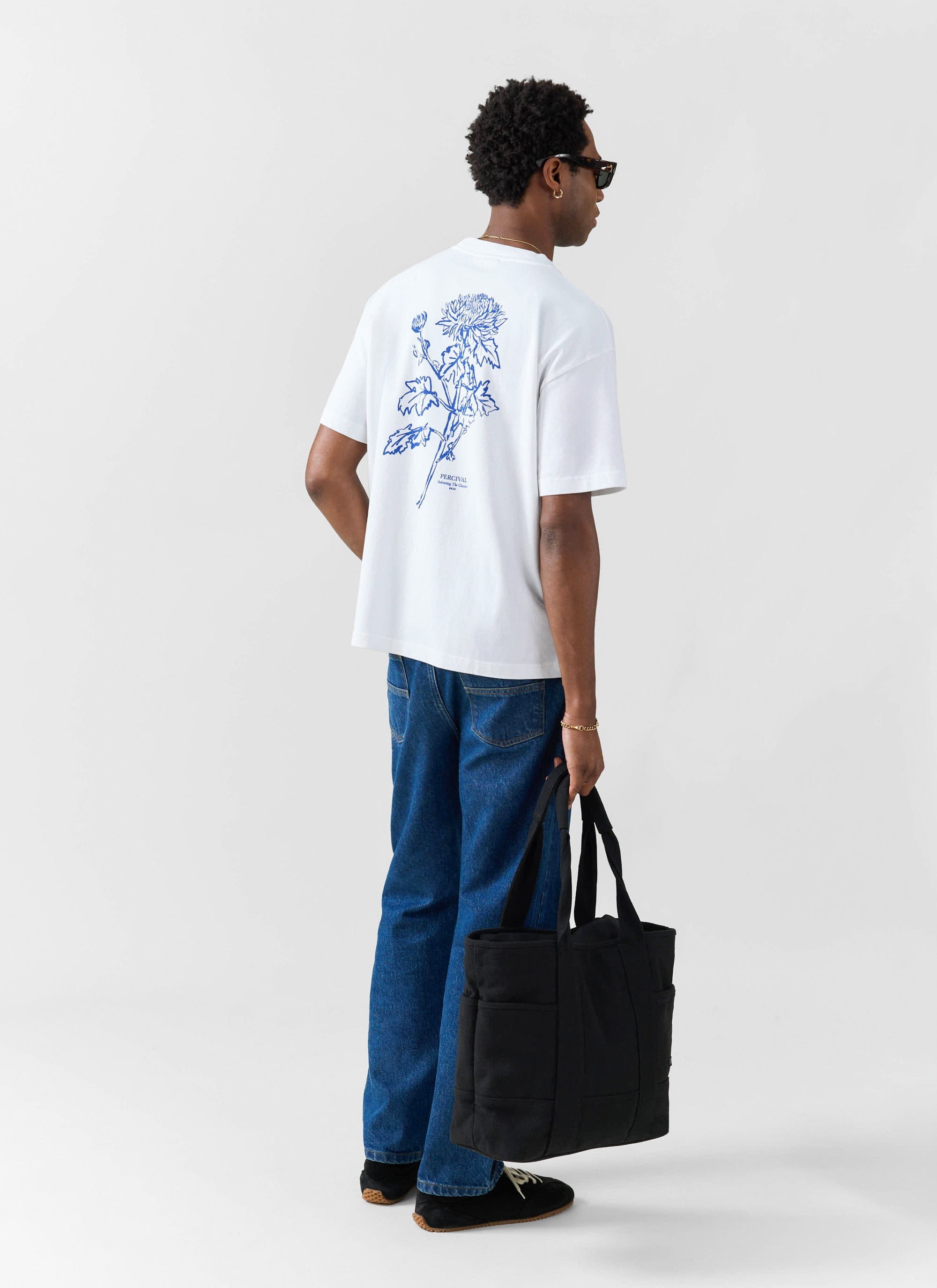 A model wears the white Percival Smith Floral T-shirt, seen from behind to showcase the blue floral back graphic.