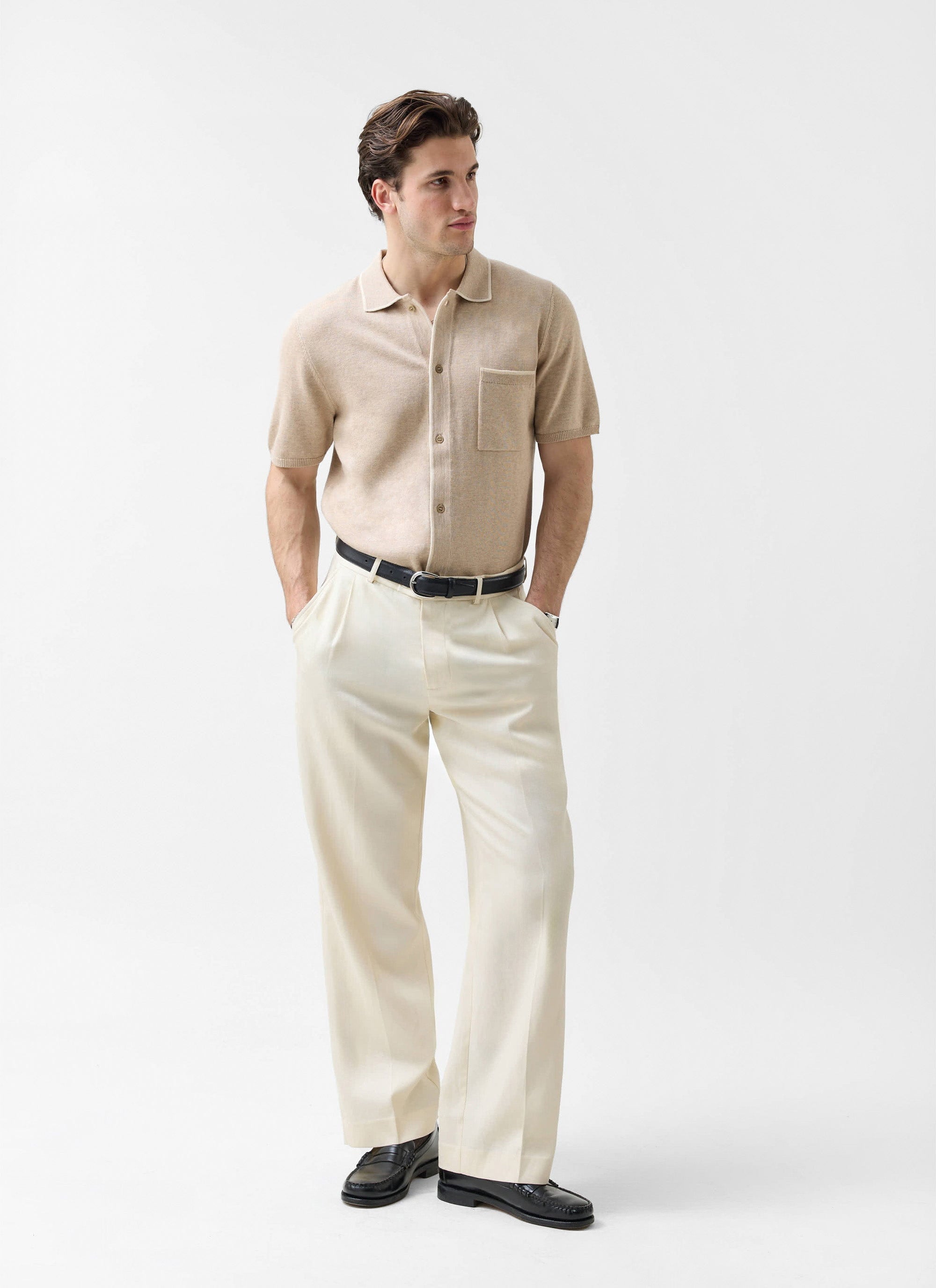 A man models the Percival Contrast Trim Regular Knitted Shirt in beige, styled with cream trousers and black loafers.