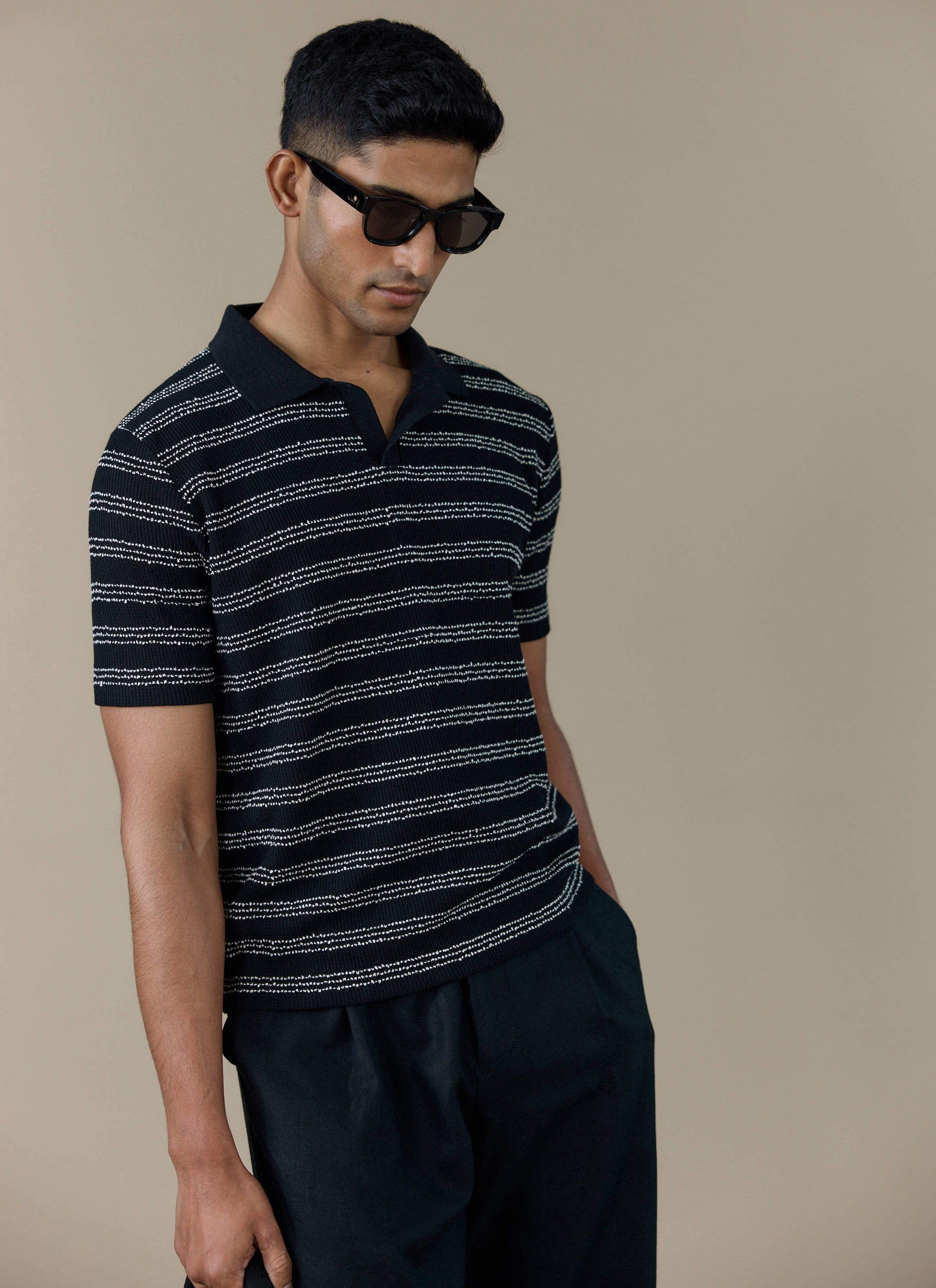 A model wearing the black Laurent Boxy Polo with textured white stripes and an open collar from Percival.