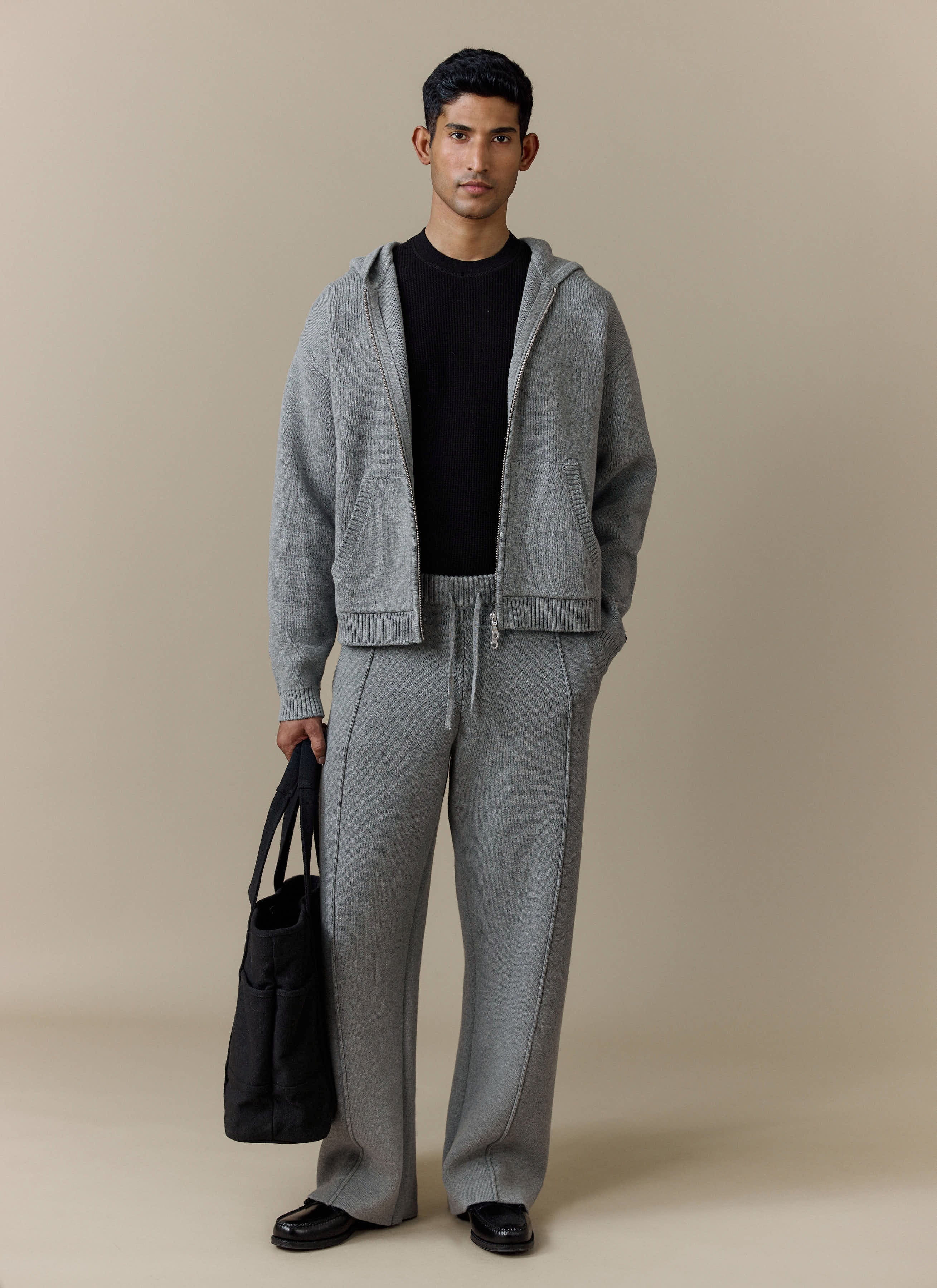 A model in a studio wearing the grey Percival Chronicle Knitted Hoodie and matching trousers as a full knitted tracksuit.