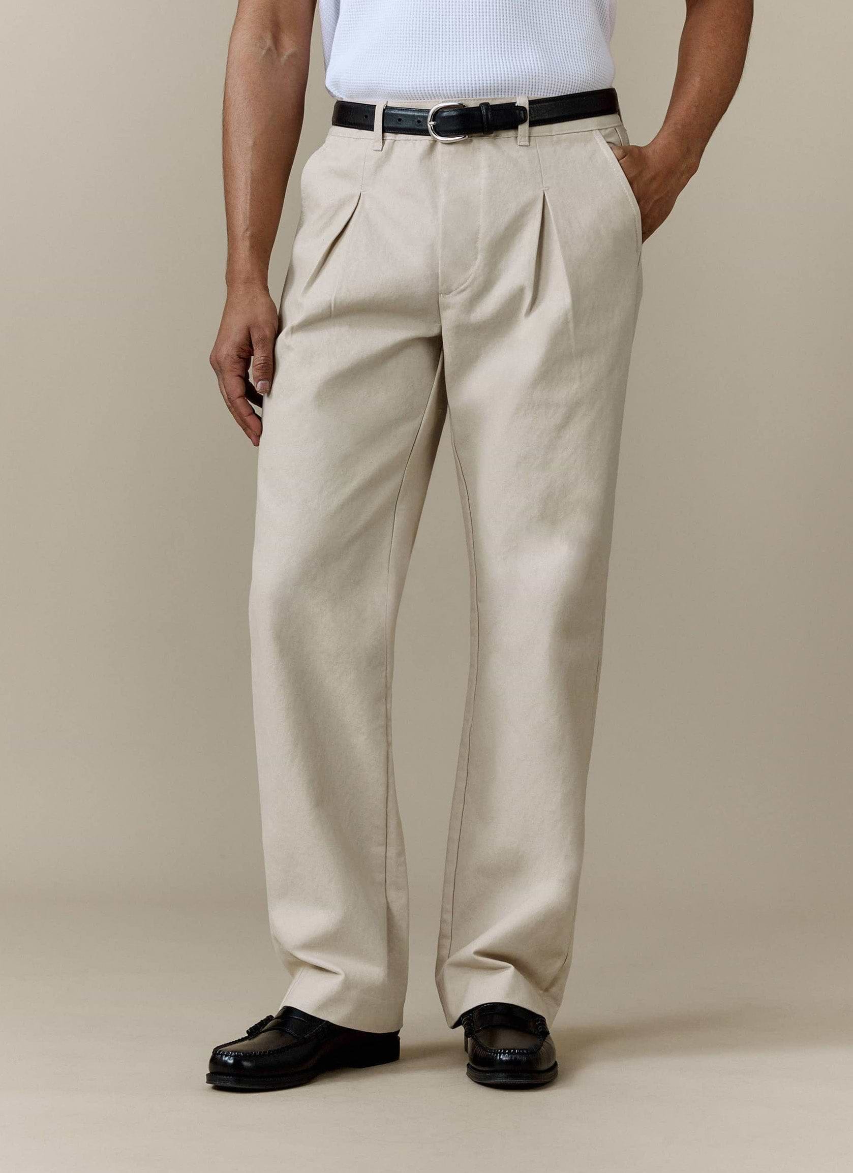 A model wears the ecru Seb Inverted Pleat Trousers by Percival, styled with a black belt and black loafers.