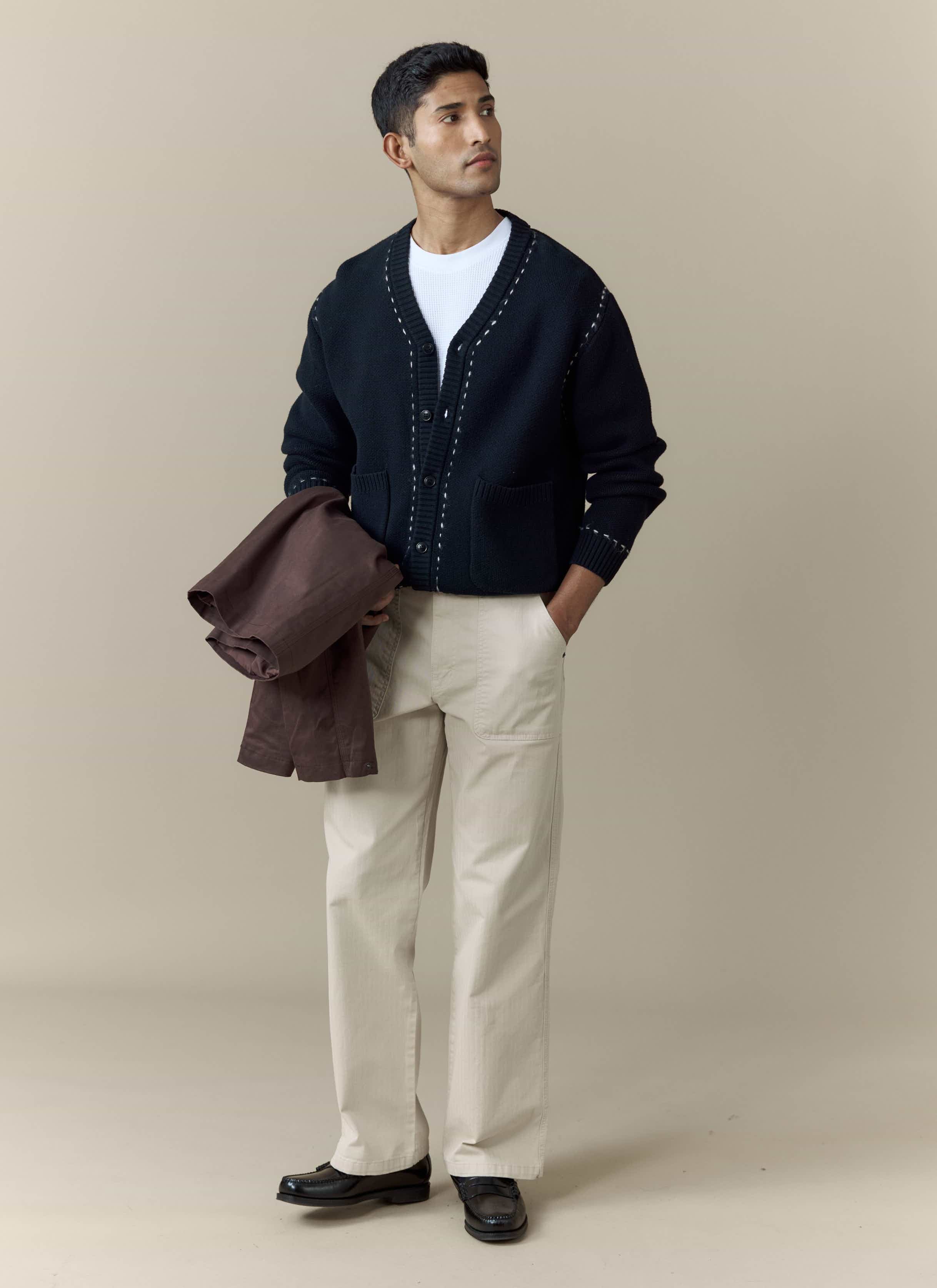 A model wears the black Module Boxy Cardigan from Percival, styled with beige trousers and a white t-shirt.