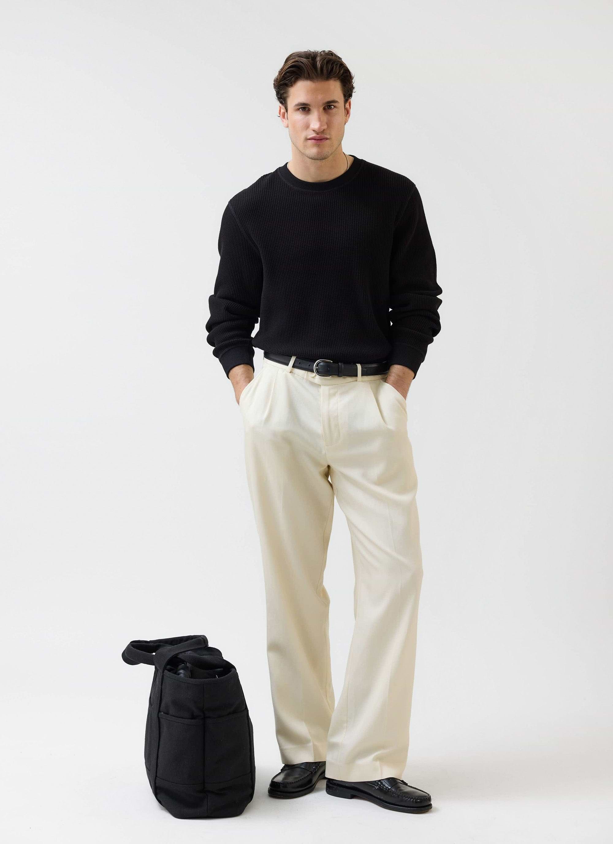 A model wears the black Waffle Long Sleeve T Shirt from Percival, styled with cream wide-leg trousers and black loafers.