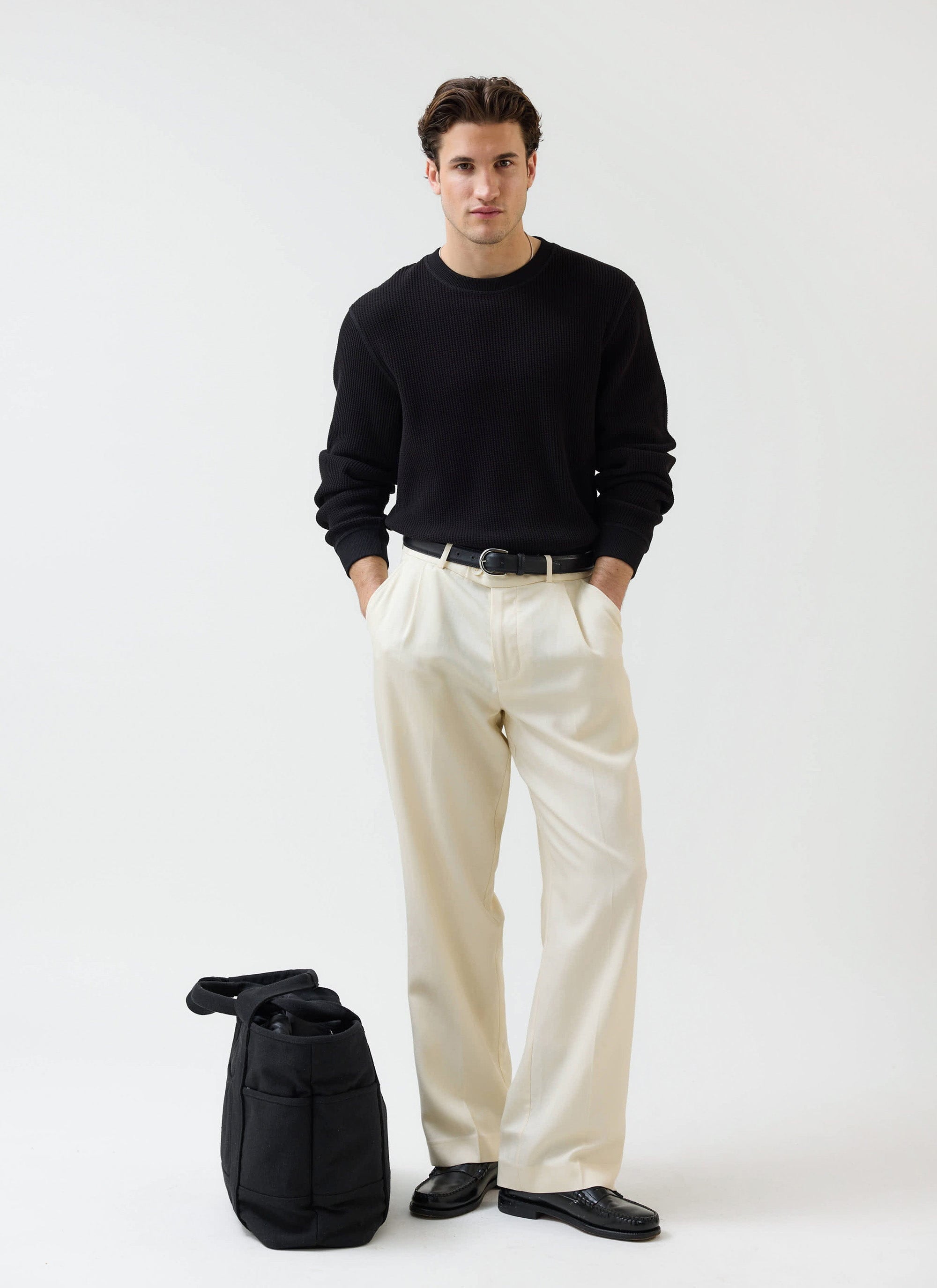 A model wears the black Waffle Long Sleeve T Shirt from Percival, styled with cream wide-leg trousers and black loafers.