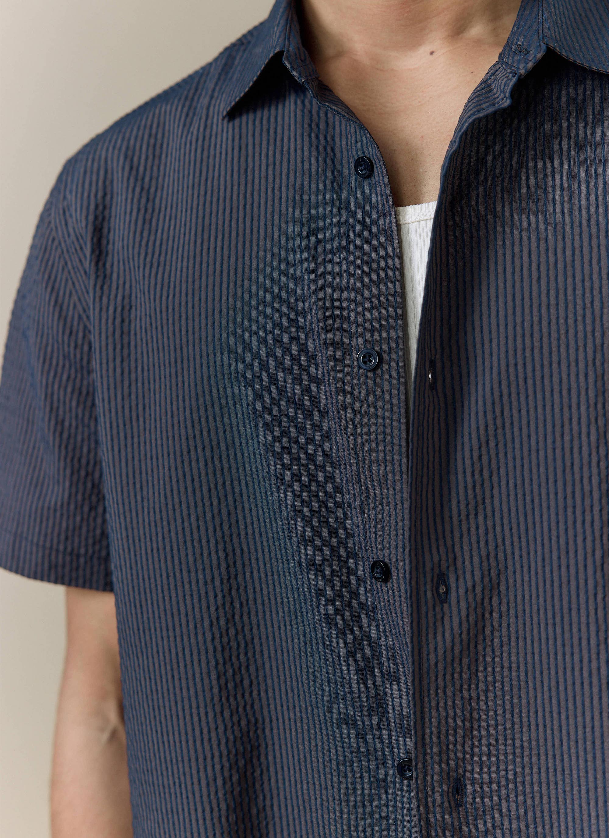 A close-up of the navy stripe Rowan Seersucker Boxy Shirt by Percival, showing the textured cotton fabric and buttons.