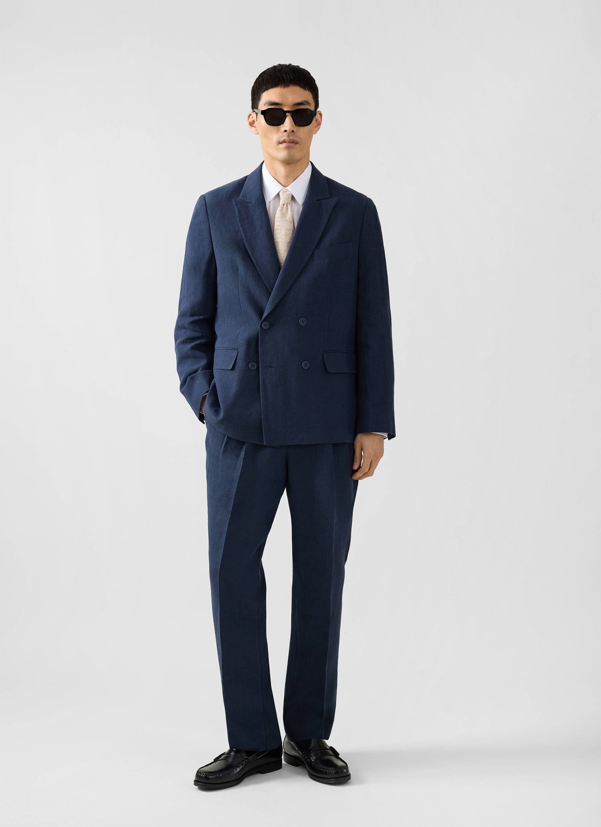 A model wears the navy linen Clifton Double Breasted Blazer from Percival, styled with matching trousers and sunglasses.