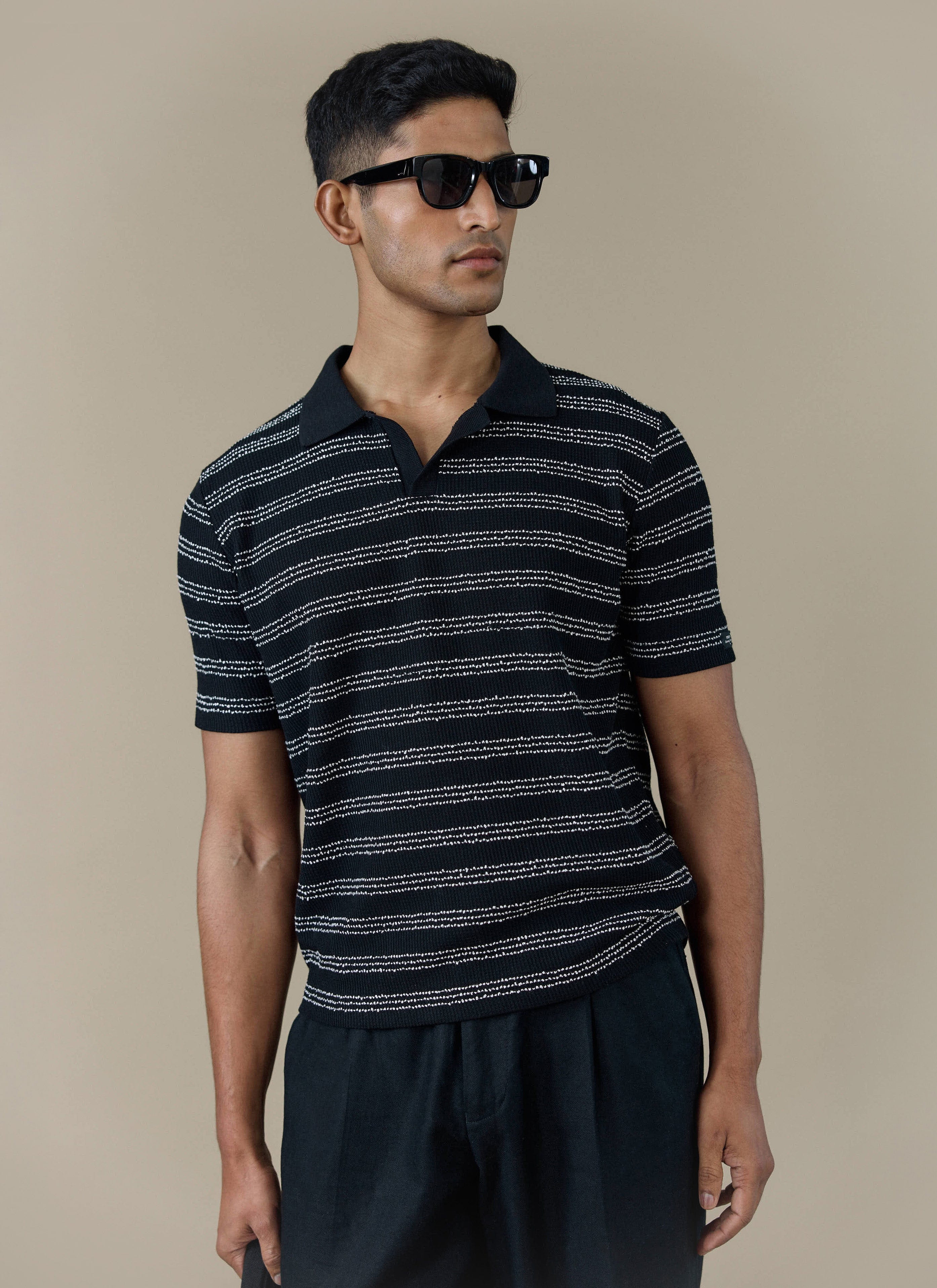 A model wearing the Percival Laurent Polo in black stripe, featuring a boxy fit and textured knit stitch.