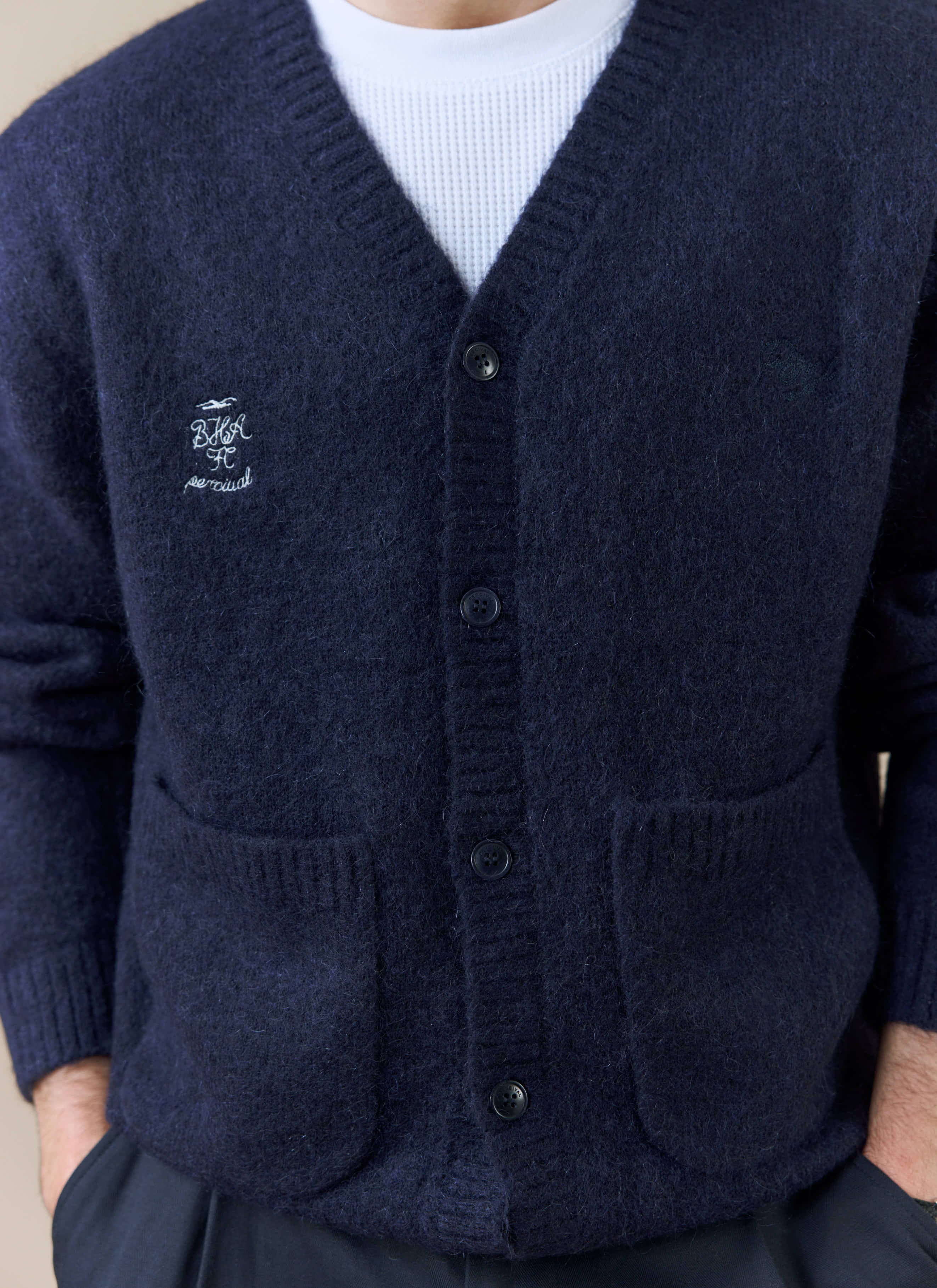 A close-up of the white chest embroidery on the navy White Glove Cardigan from the Percival x Brighton & Hove Albion F.C.
