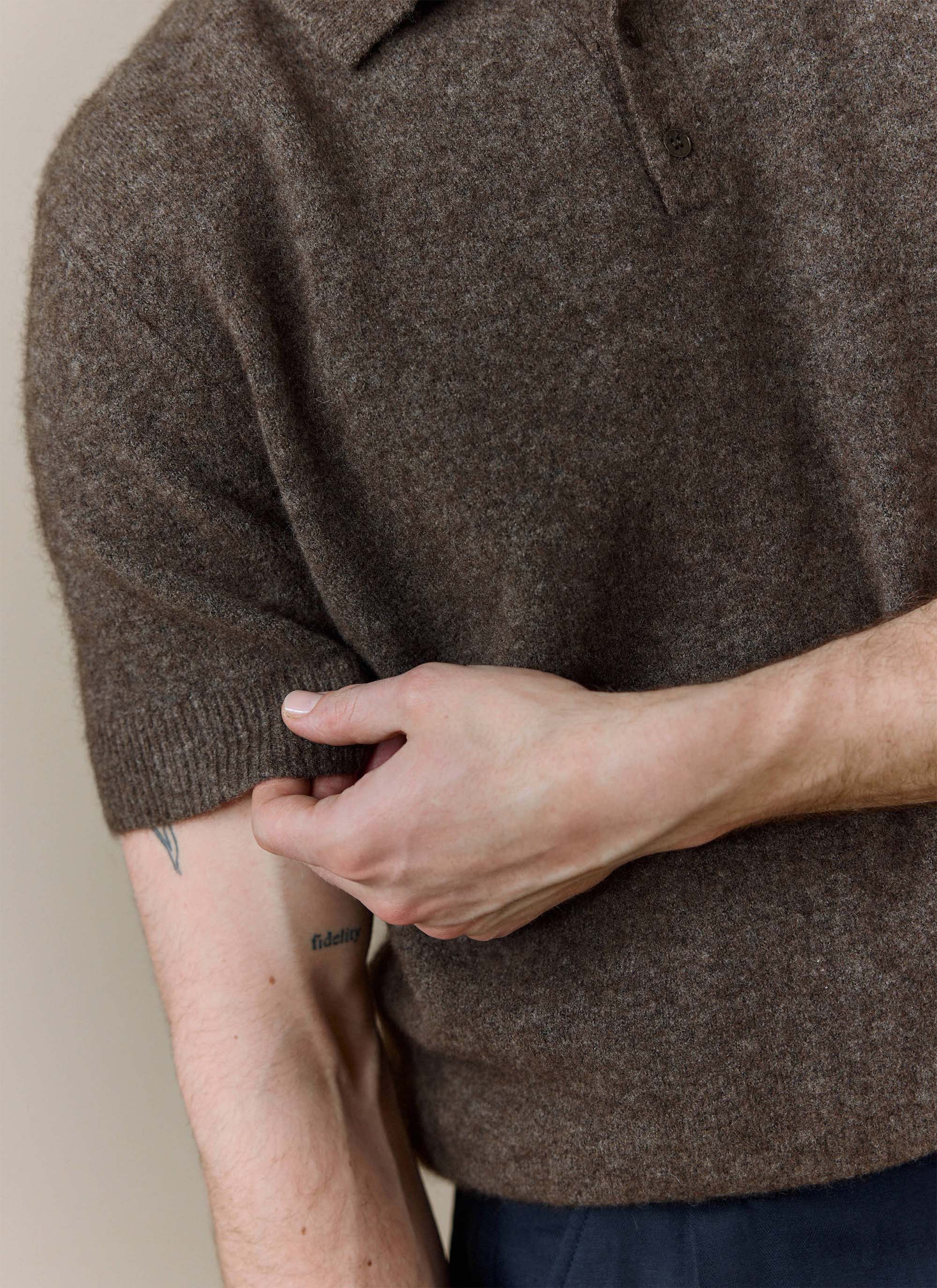 A close-up of a model adjusting the sleeve of the Percival Collins Boxy Knitted Polo in an espresso yak-wool blend.