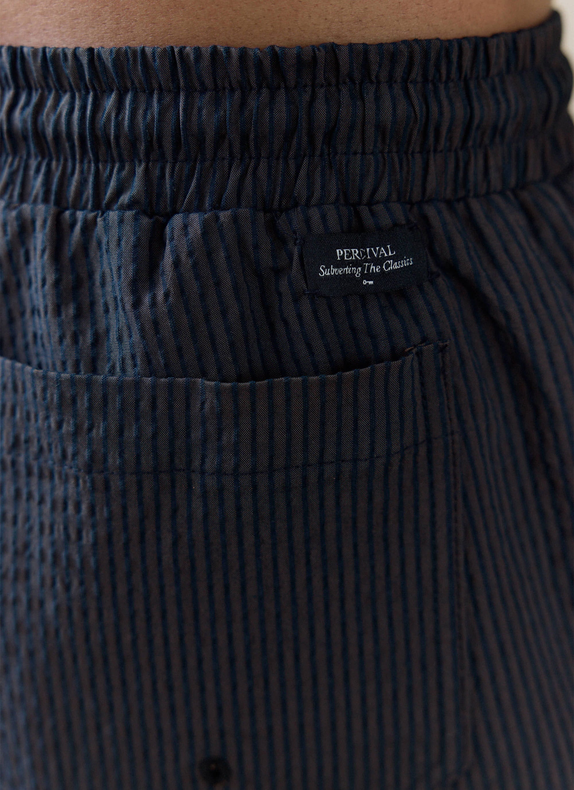 Close-up of the navy stripe seersucker cotton fabric and brand tag on the Rowan Swim Shorts by Percival.