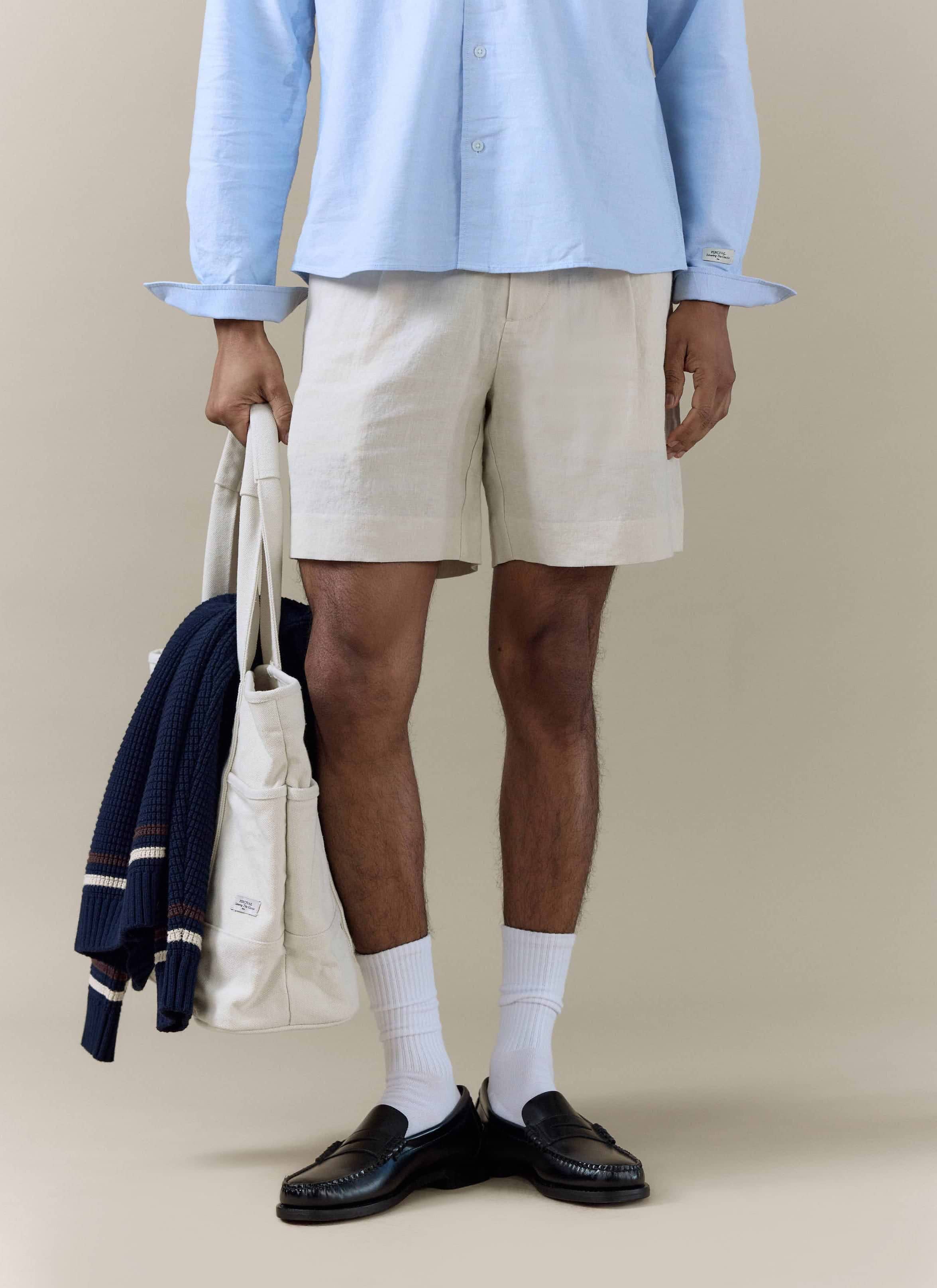 Percival pleated linen shorts in natural, styled with black loafers and a cream tote bag for a smart-casual look.