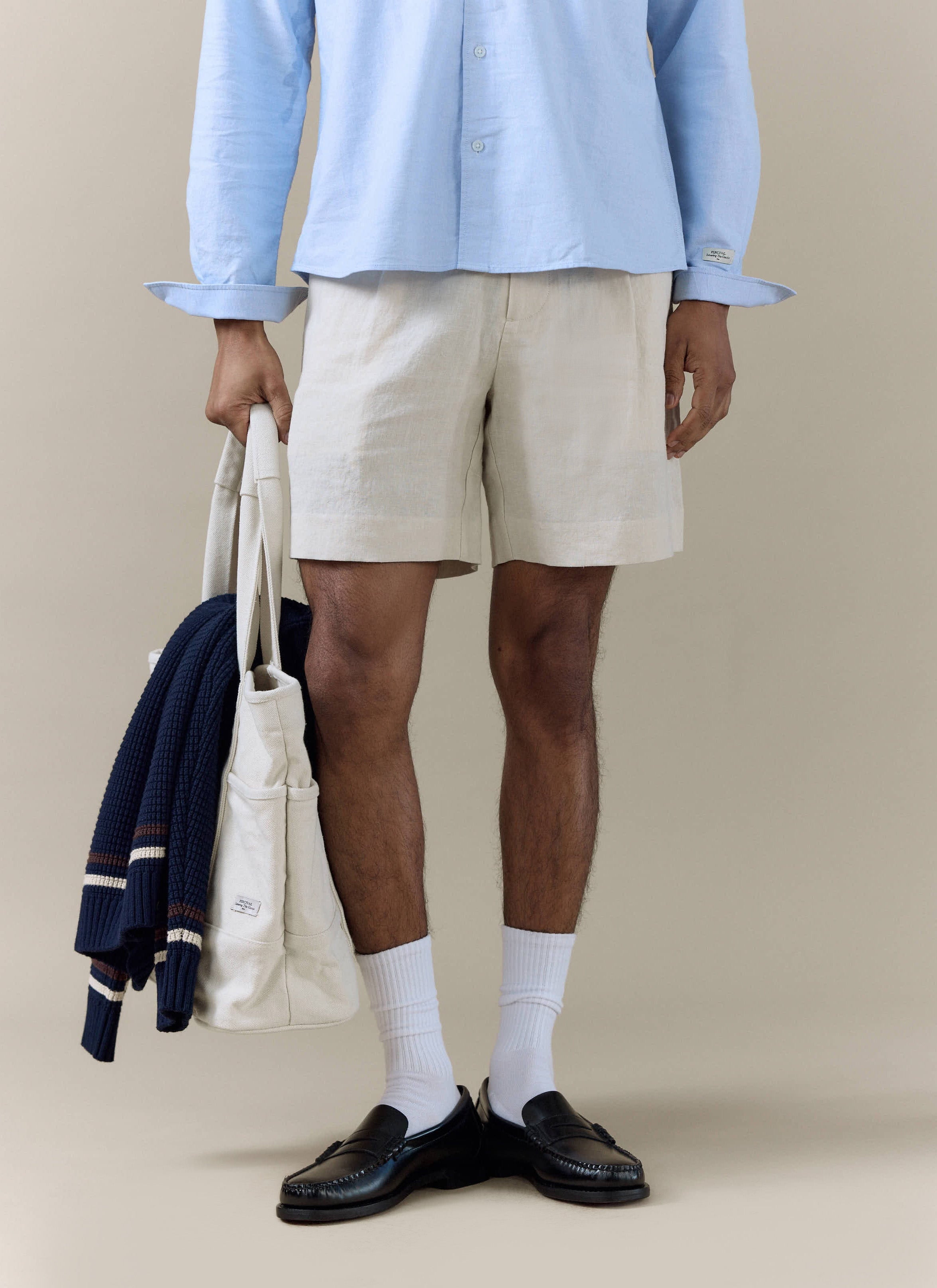 Percival pleated linen shorts in natural, styled with black loafers and a cream tote bag for a smart-casual look.