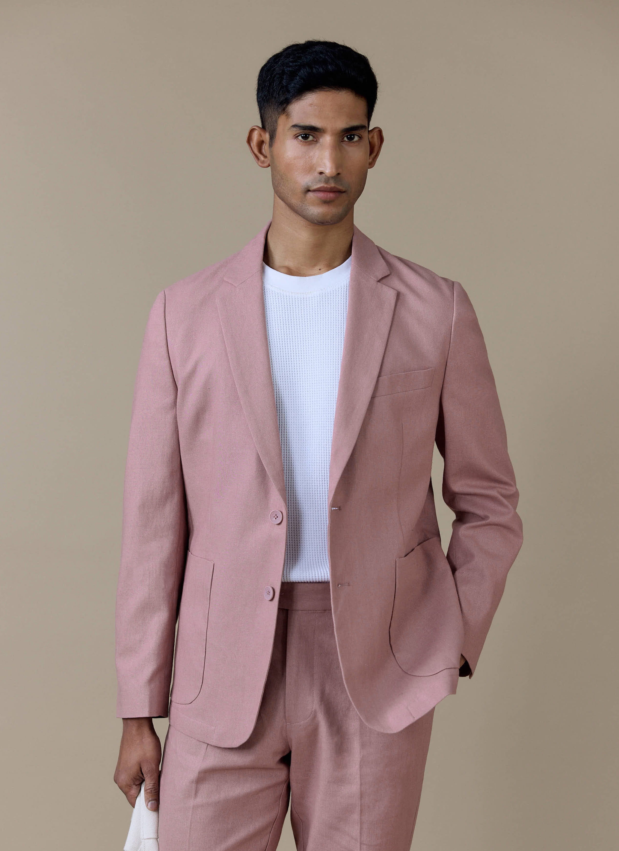 Tailored linen blazer in dusty pink by Percival, styled over a white knit top with matching tailored trousers.