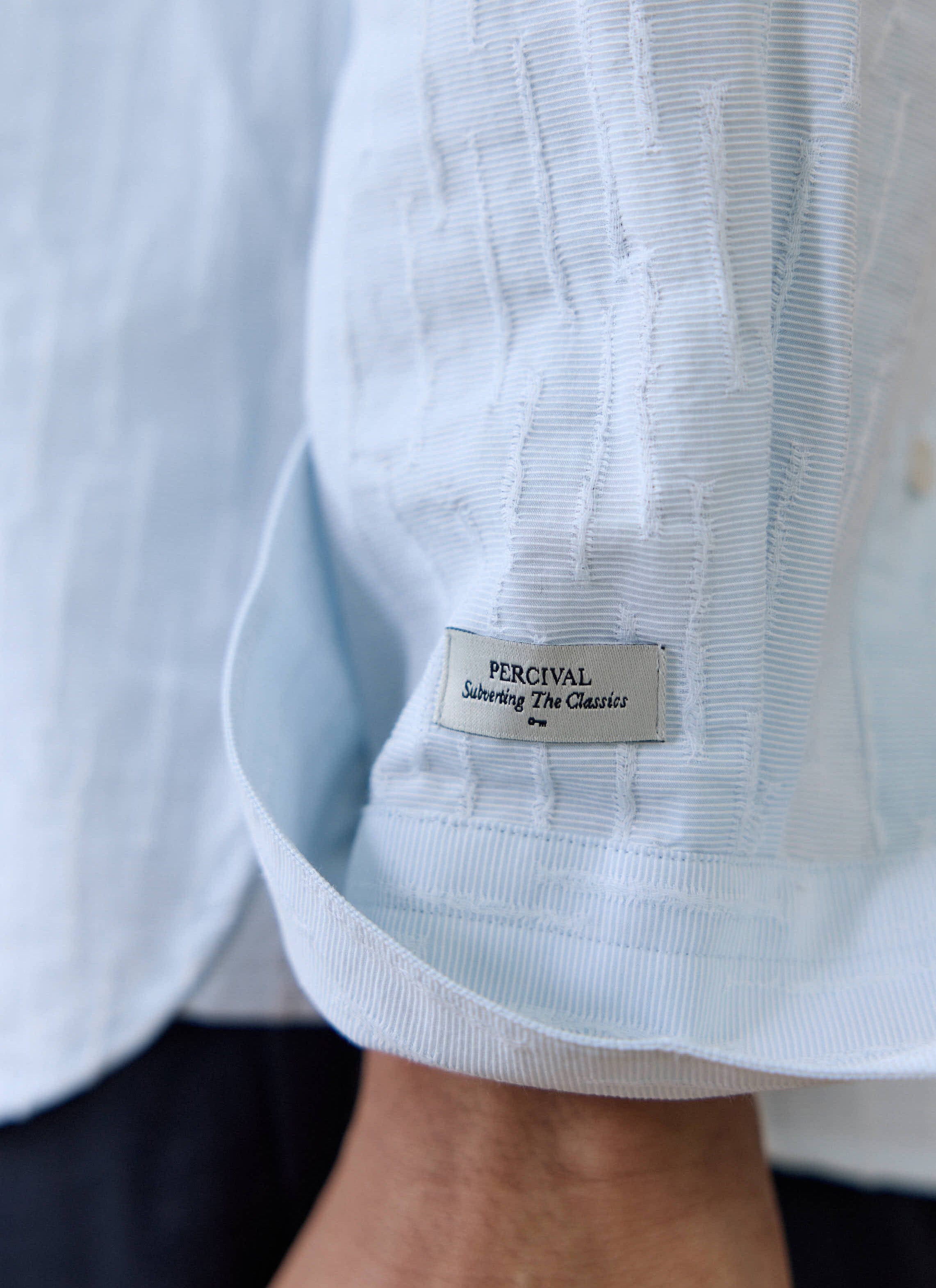 Close-up of the light blue Percival Paros Pearce Shirt, showing the textured seersucker fabric and brand label.