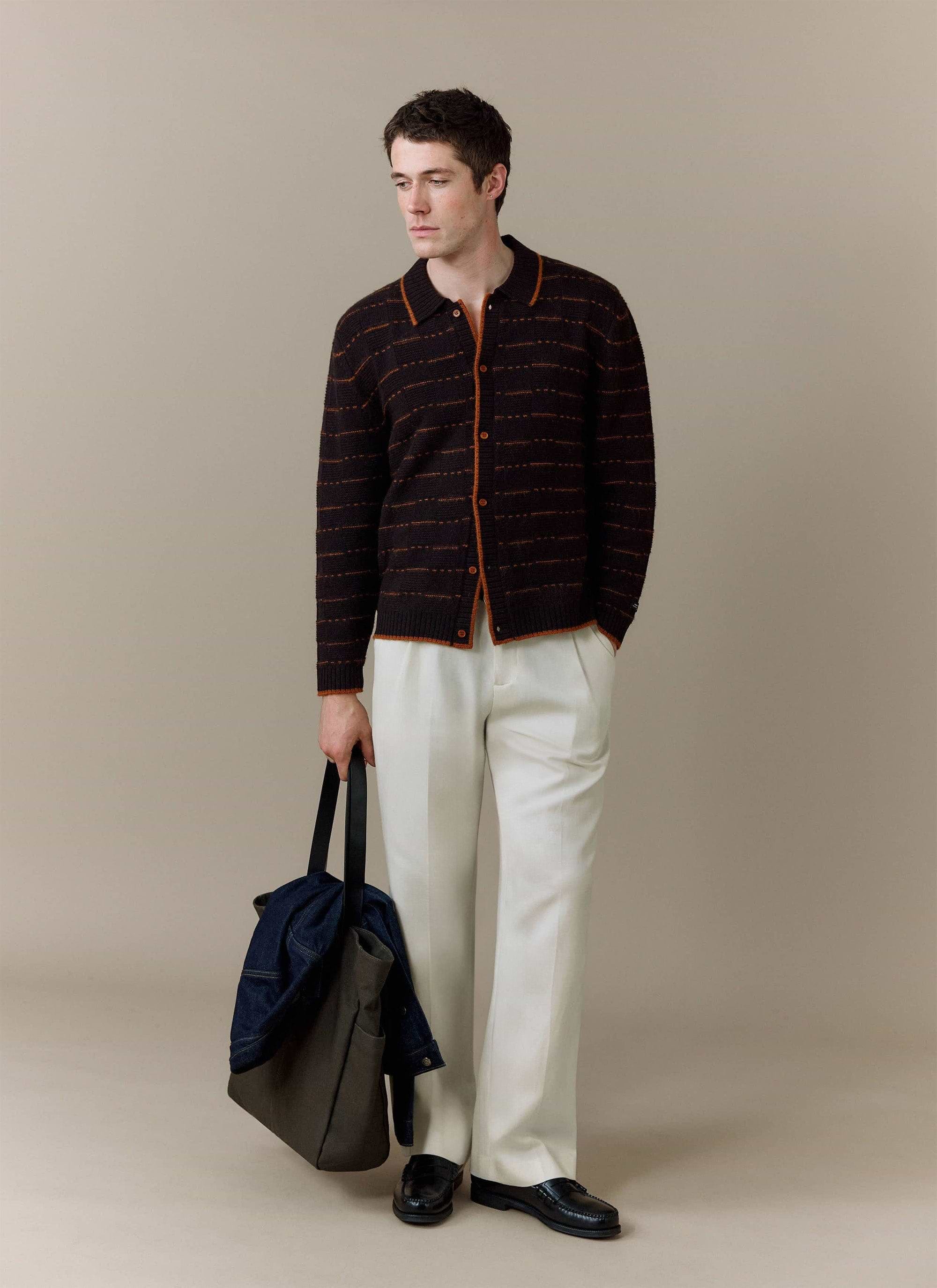 A model wears the brown Addison Knitted Shirt from Percival, styled with white trousers and carrying a tote bag.