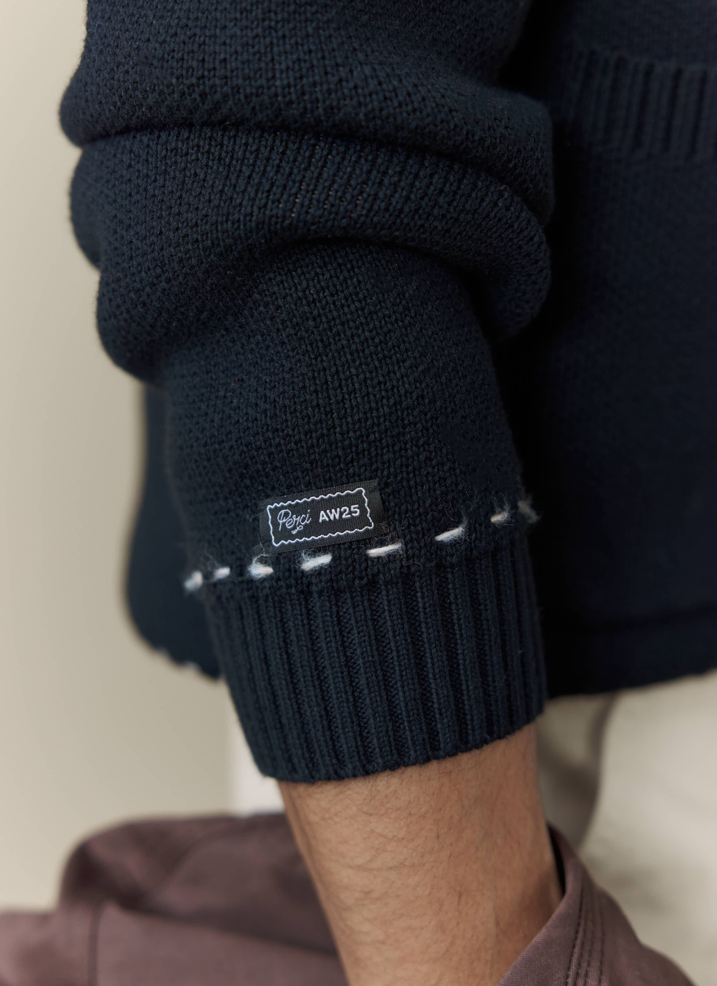 A close-up shot of the cuff on the black Percival Module Boxy Cardigan, showing the brand label and decorative stitching.