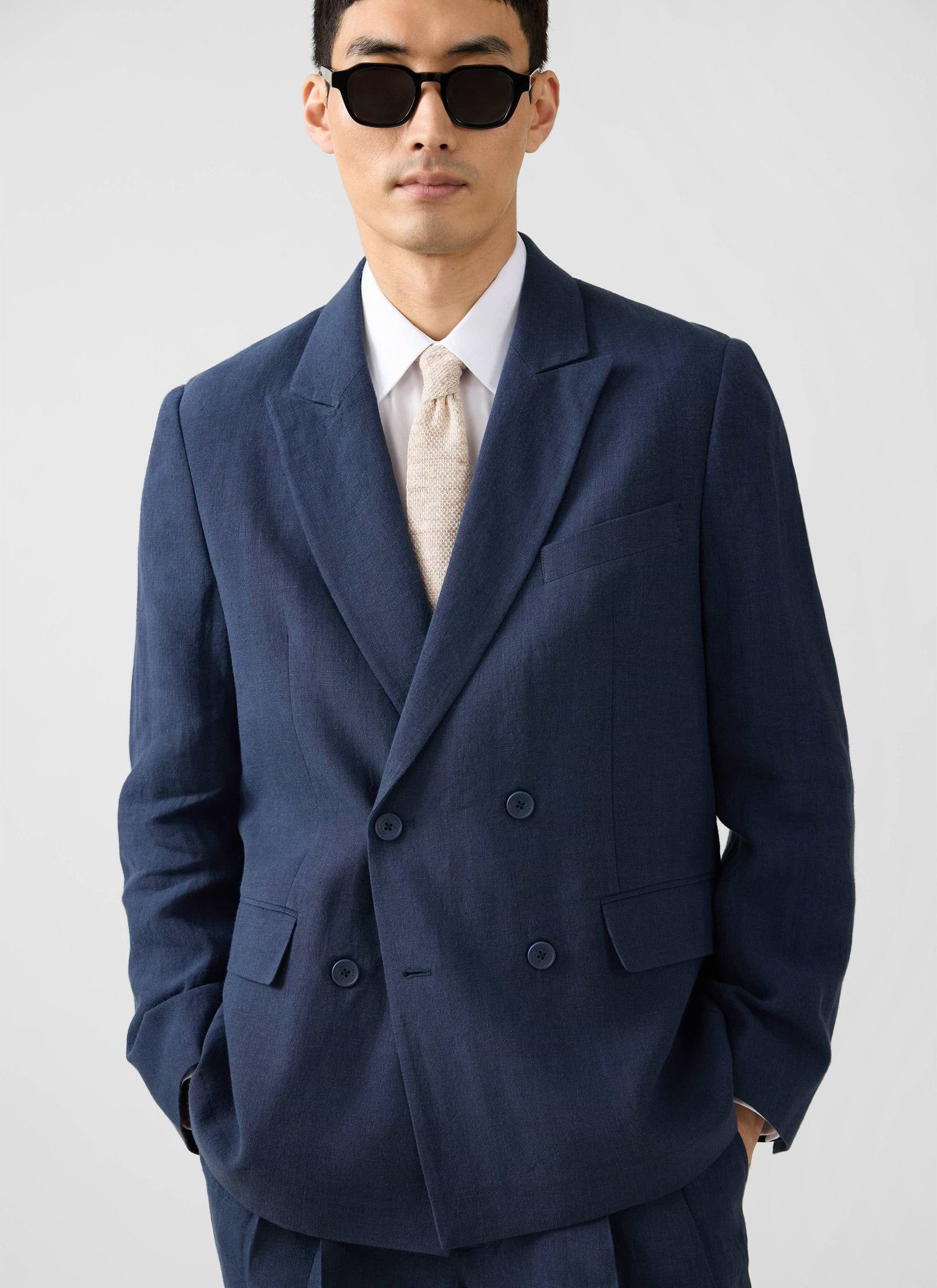 A model wears the Percival Clifton Double Breasted Blazer in navy linen, styled with a white shirt, cream tie & sunglasses.