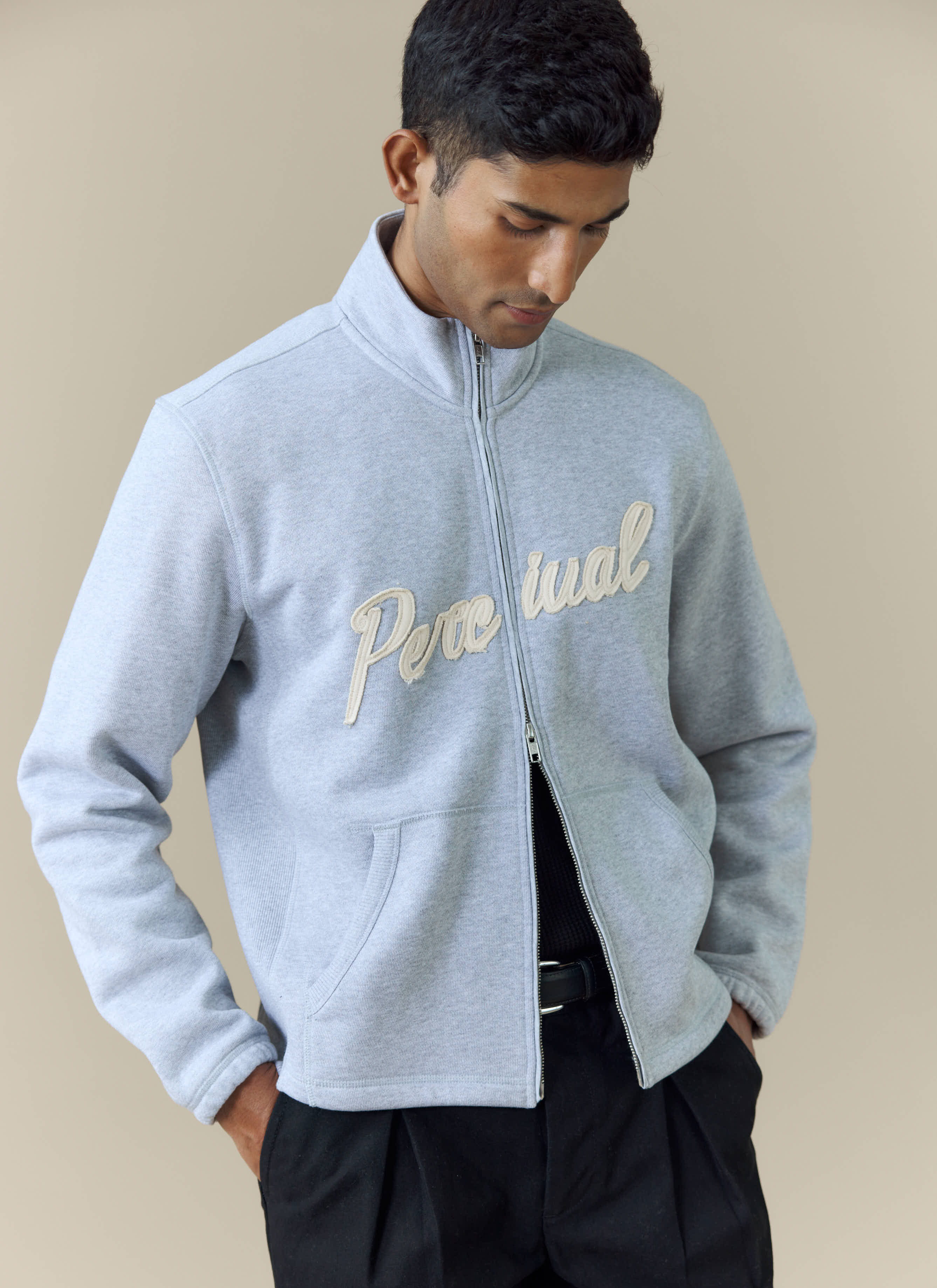 A model wearing the Percival Curtis Boxy Zip Funnel Neck Sweatshirt in Athletic Grey with cream script logo embroidery.