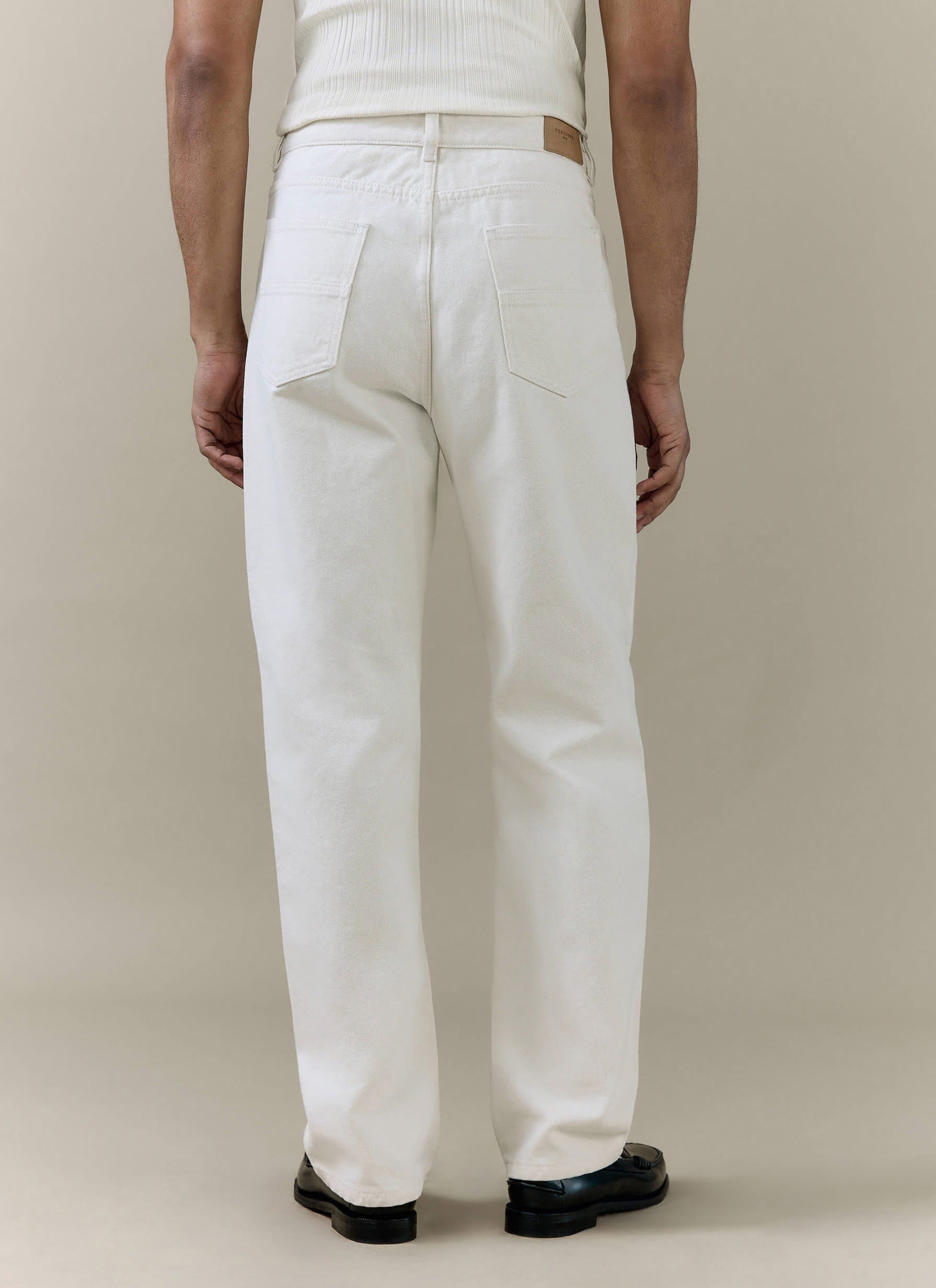 Cream straight leg denim jeans by Percival, shown from the back with two pockets and a tan leather waistband patch.