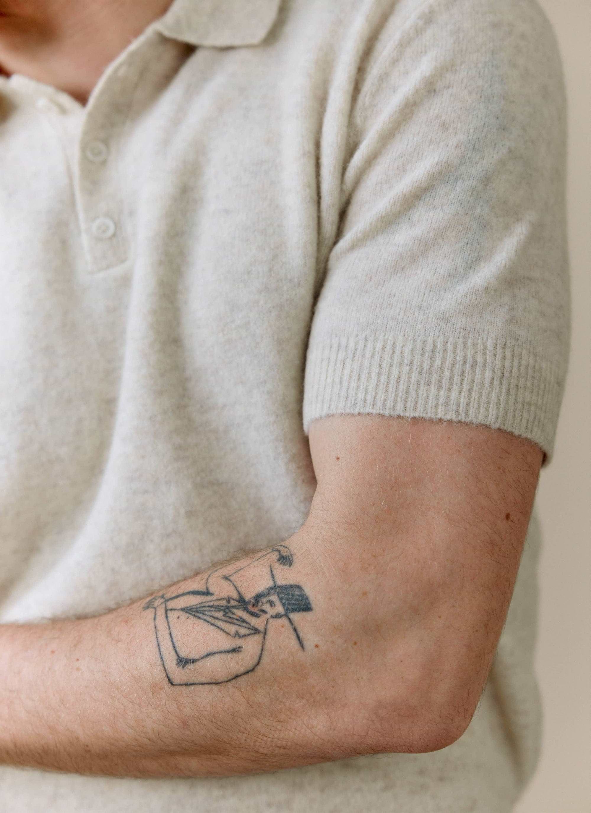 Close up of a model wearing the ecru Collins Boxy Knitted Polo from Percival, showing the soft yak blend and ribbed sleeve.