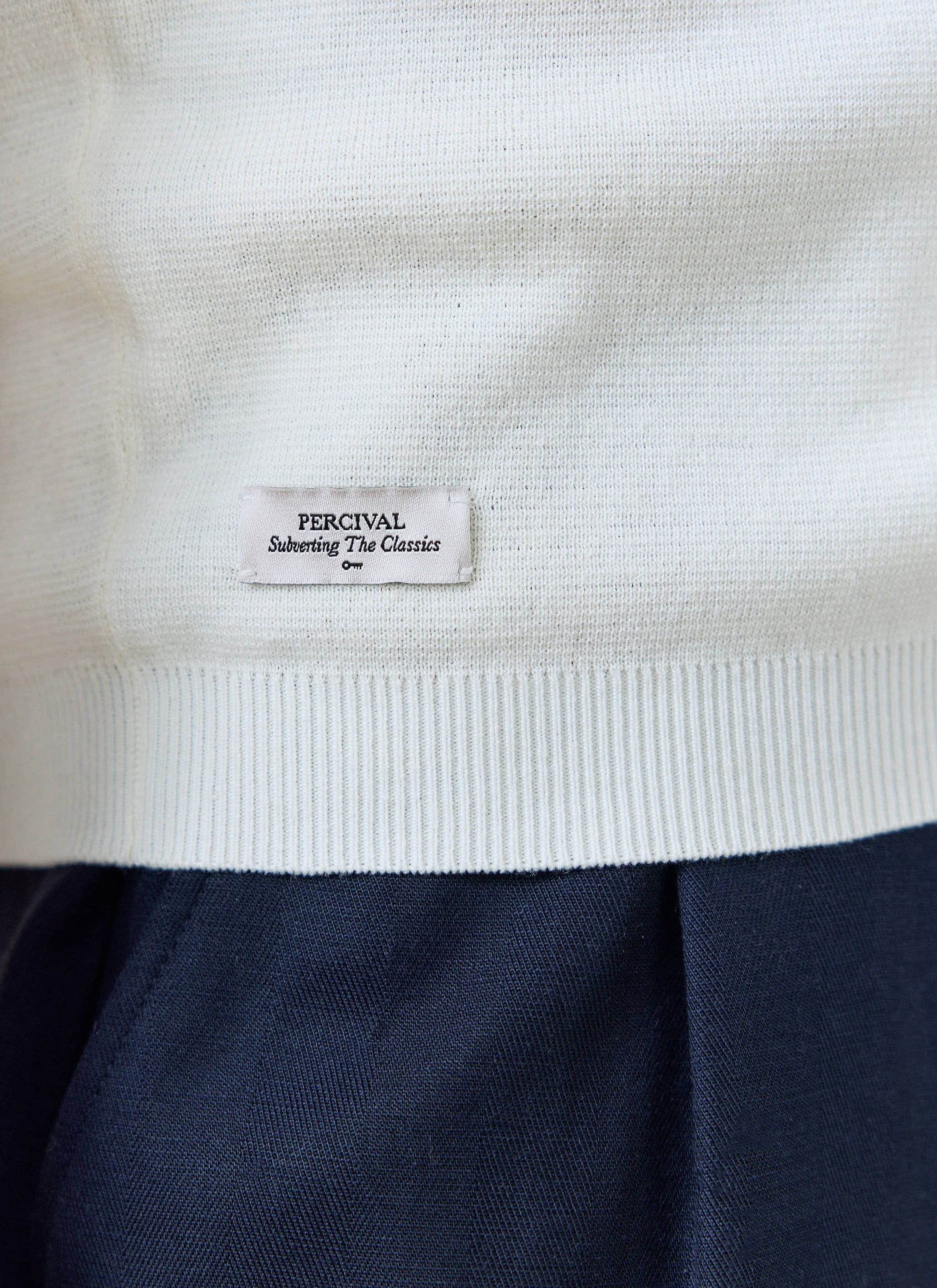 Close-up of the cream Percival Laurence Knitted Polo hem, showing the branded tab and fine linen-blend knit.