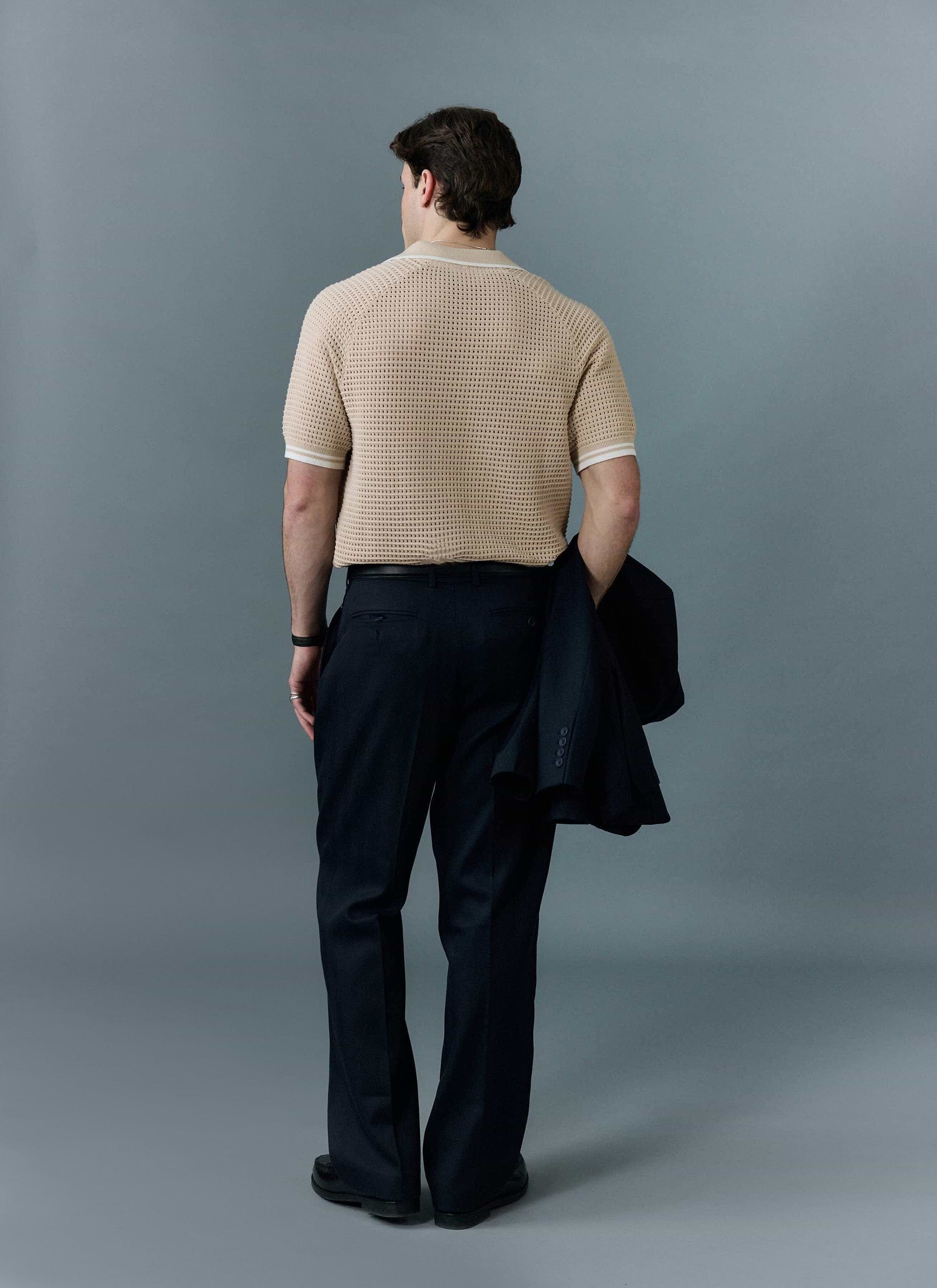 A back view of a model wearing the Percival Tennis Boxy Knitted Polo in ecru, showcasing its unique perforated texture.