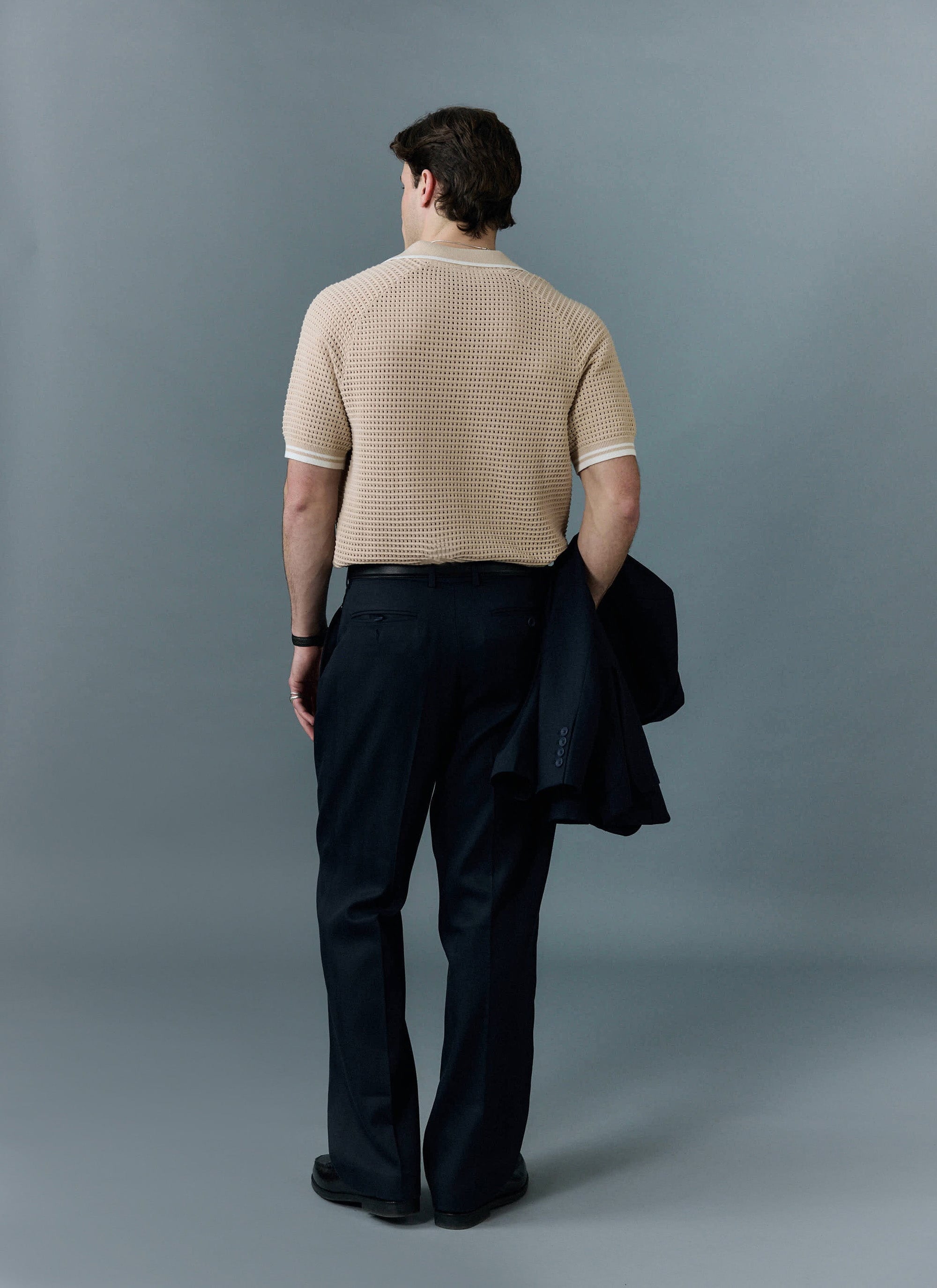 A back view of a model wearing the Percival Tennis Boxy Knitted Polo in ecru, showcasing its unique perforated texture.