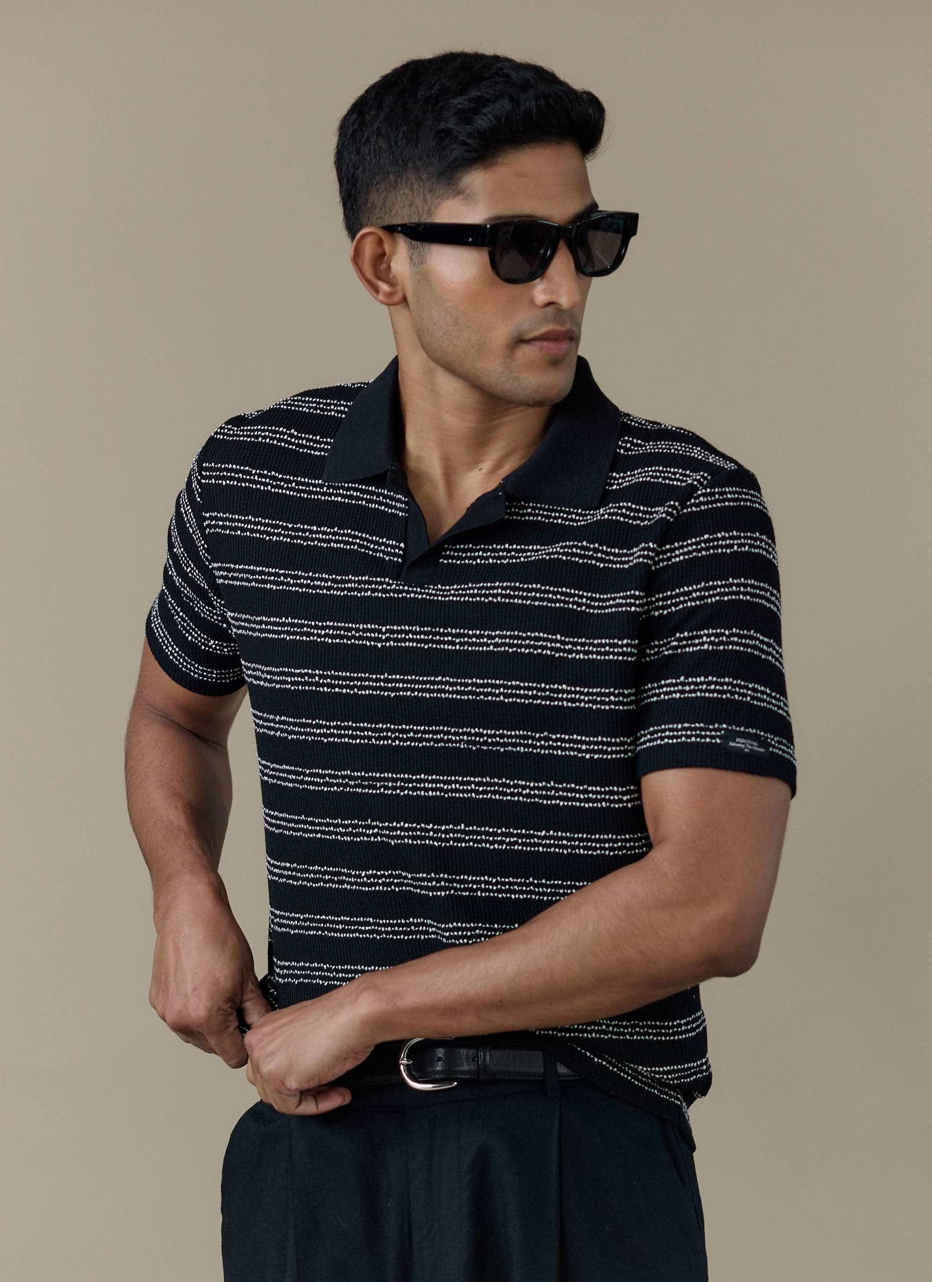 A model wearing the Percival Laurent Boxy Polo in black stripe, featuring a textured stitch and an open collar.
