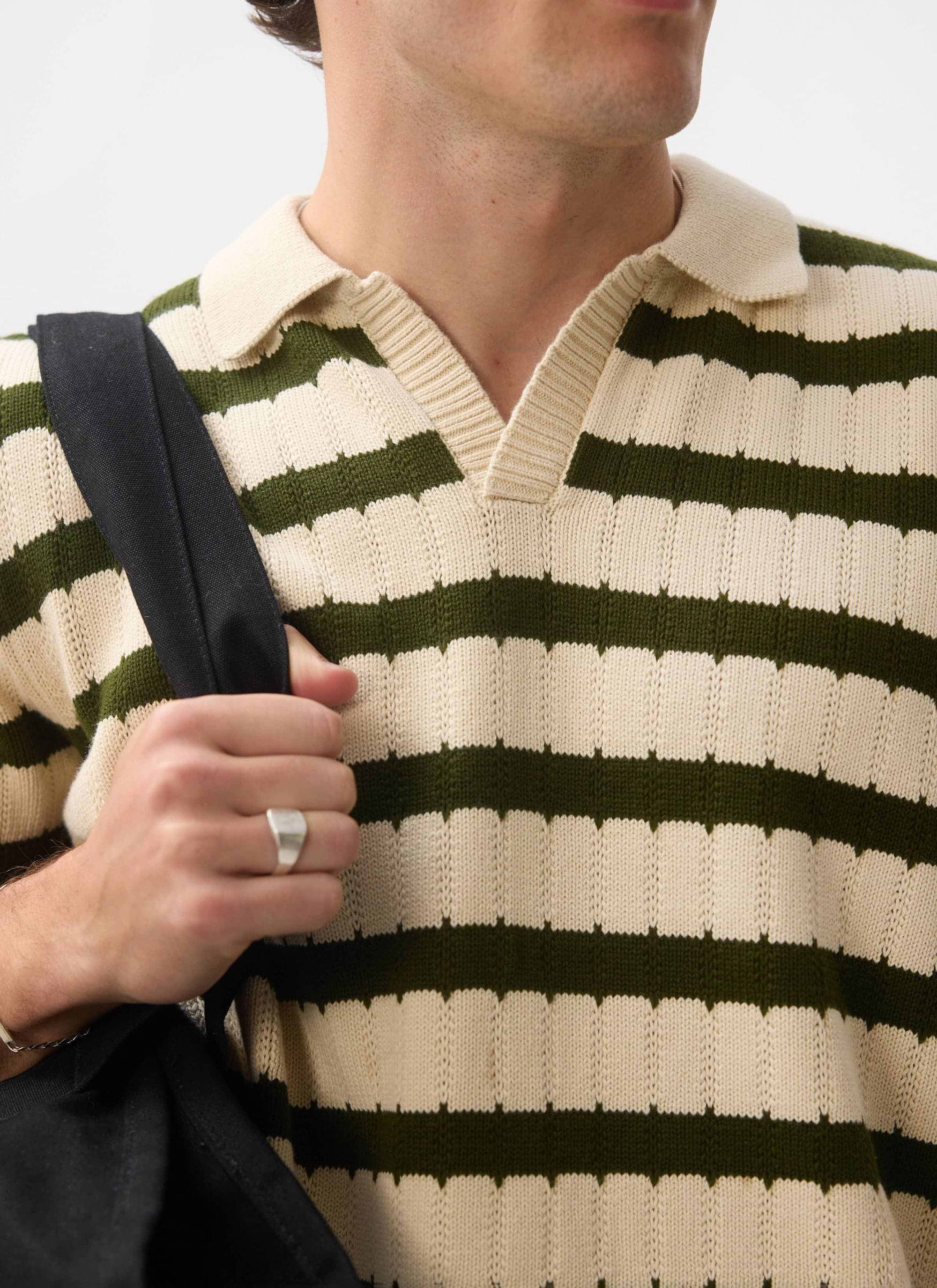 A close-up of a model wearing the Percival Stine Knitted Polo in ecru, showing the green striped jacquard knit.