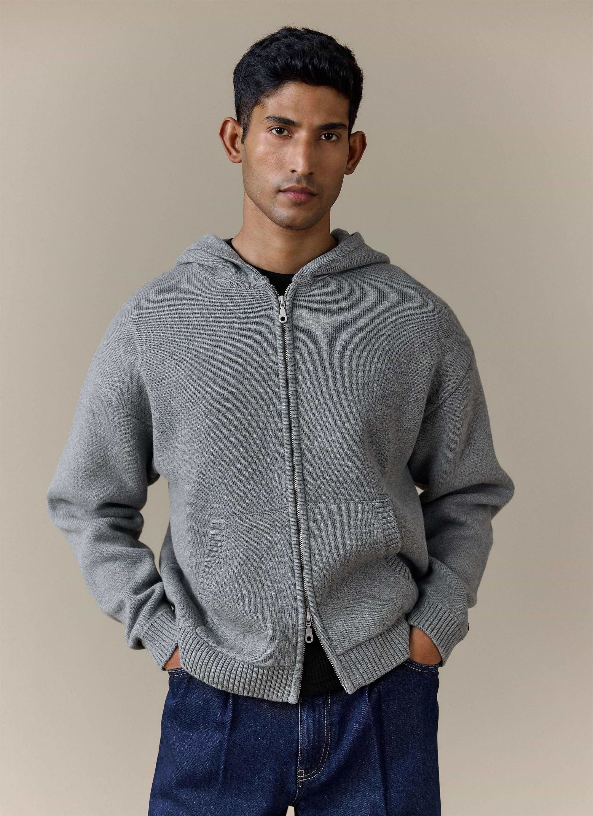 A model wears the grey Chronicle Knitted Hoodie from Percival with dark jeans, showing the zip front and kangaroo pocket.
