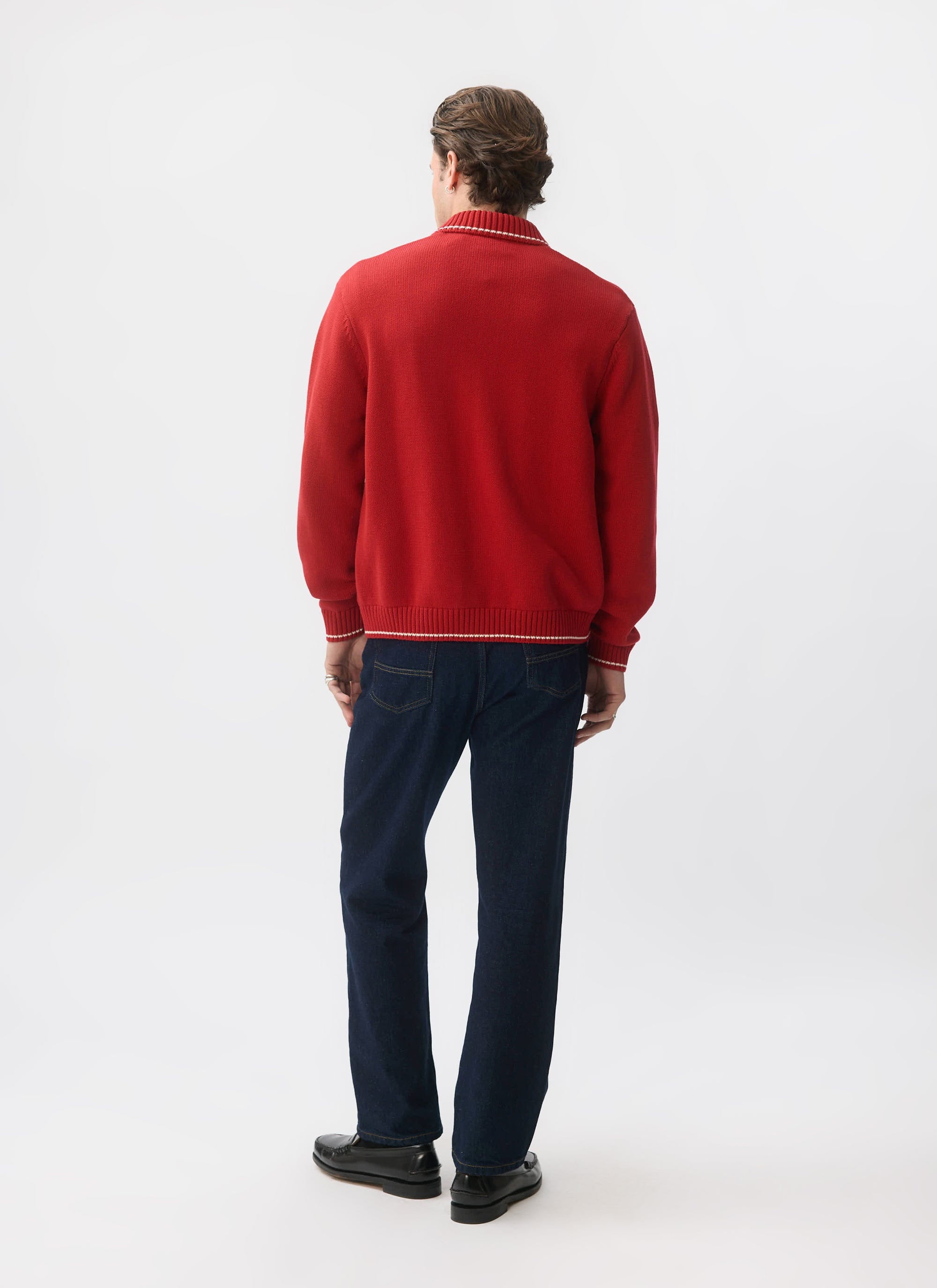 A model, seen from behind, wears the Percival Gardner Dense Knitted Zip Cardigan in red with dark jeans and loafers.
