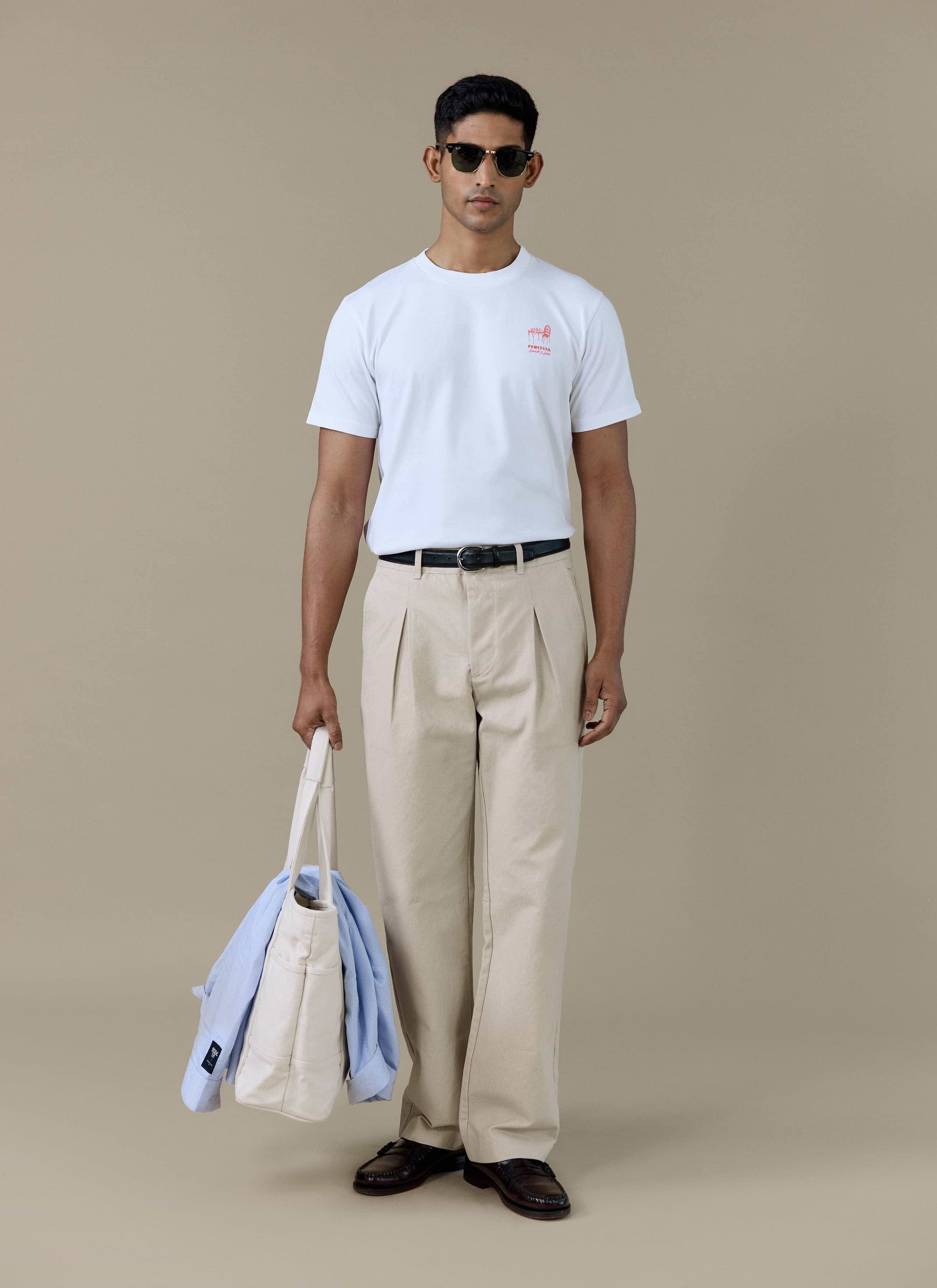 Model wearing the Percival Perci Fine Wines T-shirt in white organic cotton, styled with beige trousers and sunglasses.