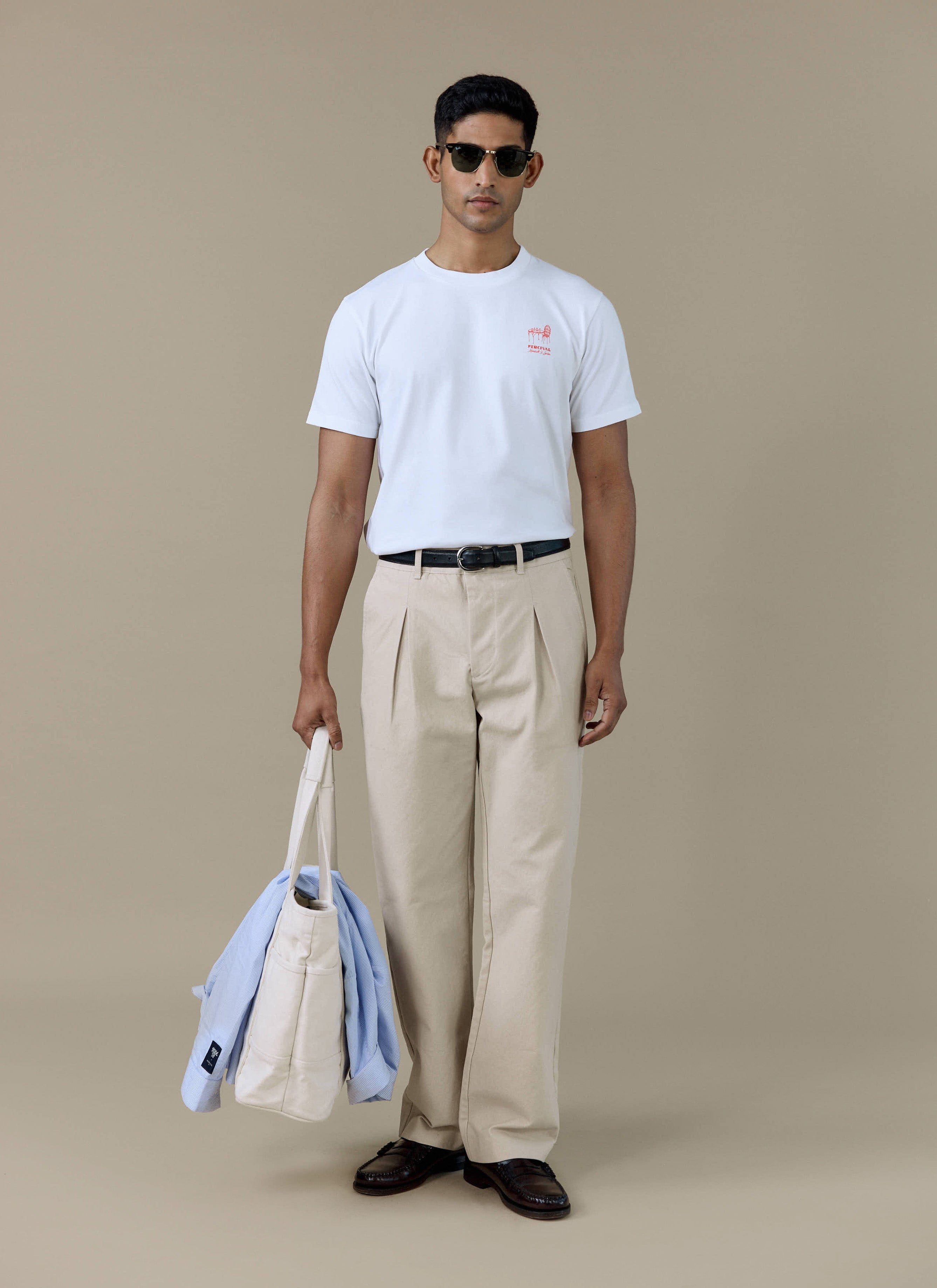 Model wearing the Percival Perci Fine Wines T-shirt in white organic cotton, styled with beige trousers and sunglasses.