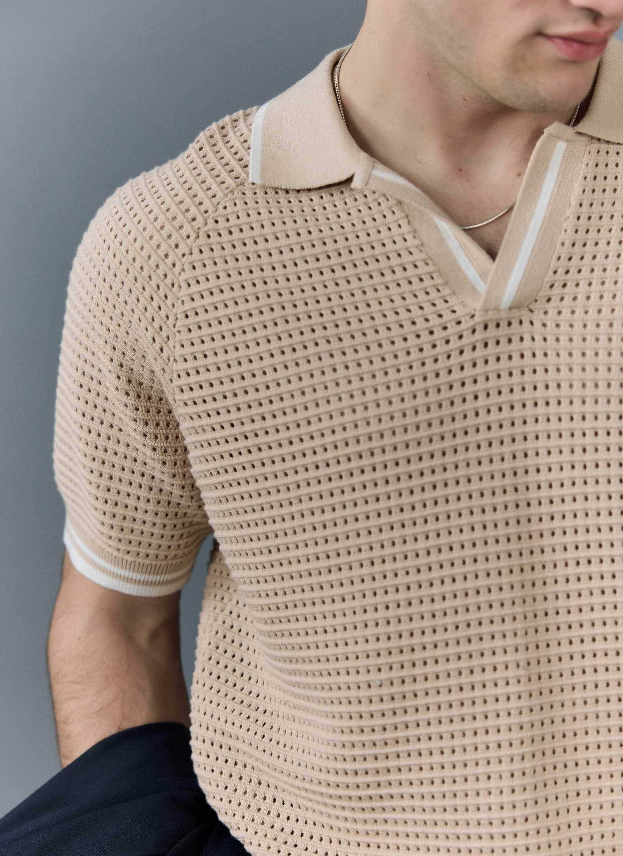 A close-up of a model wearing the Percival Tennis Boxy Knitted Polo in ecru, showing the perforated knit and striped collar.