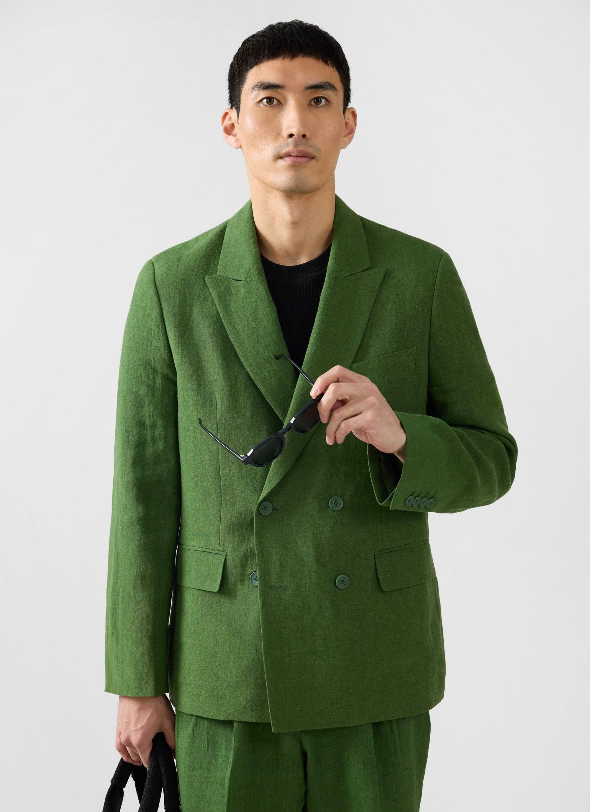 Model wearing the Percival Clifton double-breasted blazer in forest green linen, holding black sunglasses.