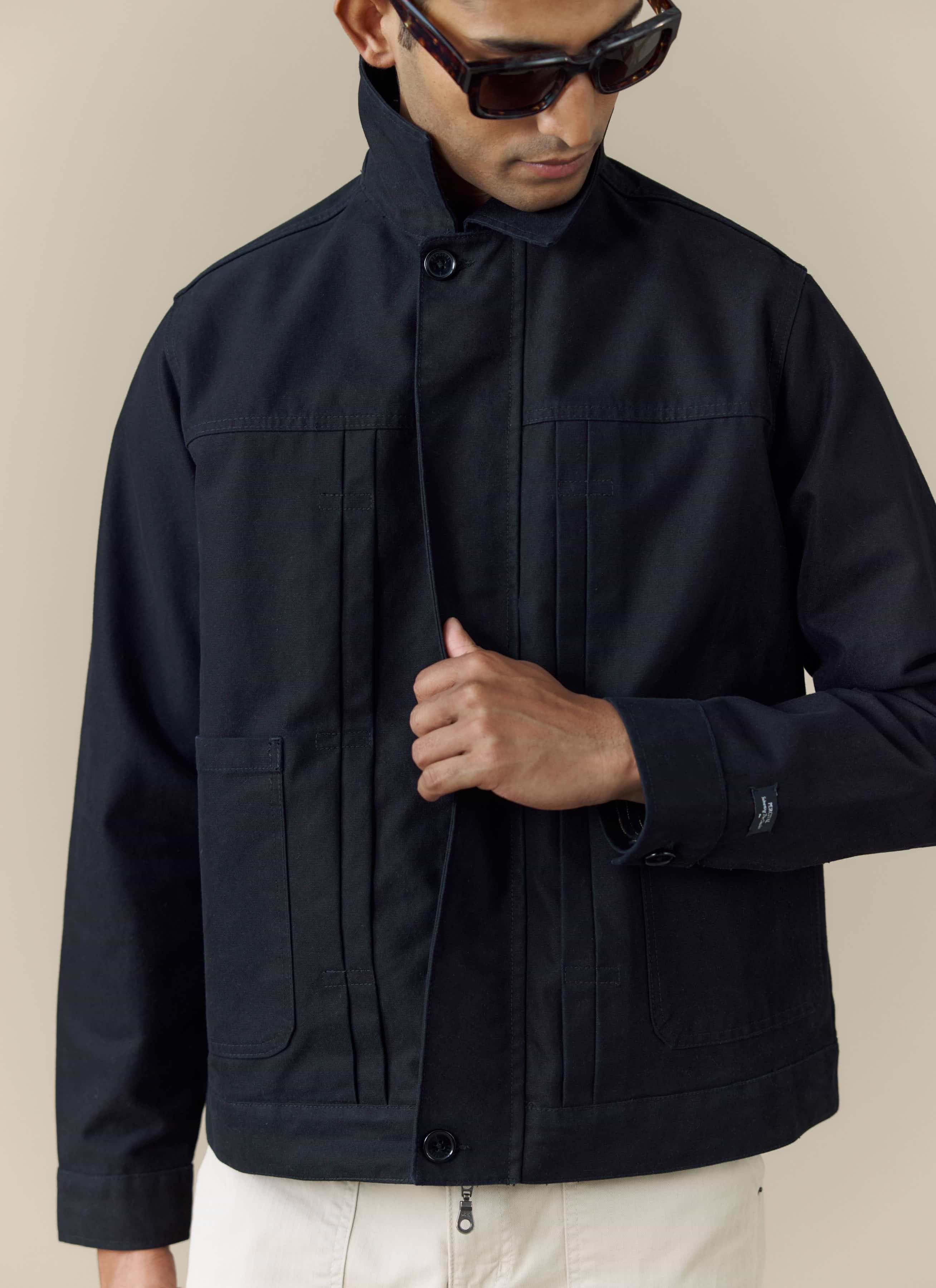 A close-up shot of a model wearing the black Percival Ernst Jacket, with the collar buttoned and styled with sunglasses.
